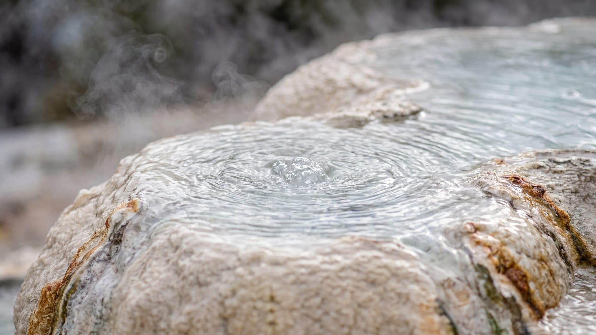 Close view of clear water welling up over pale stone, steam lifting off the surface in cold air