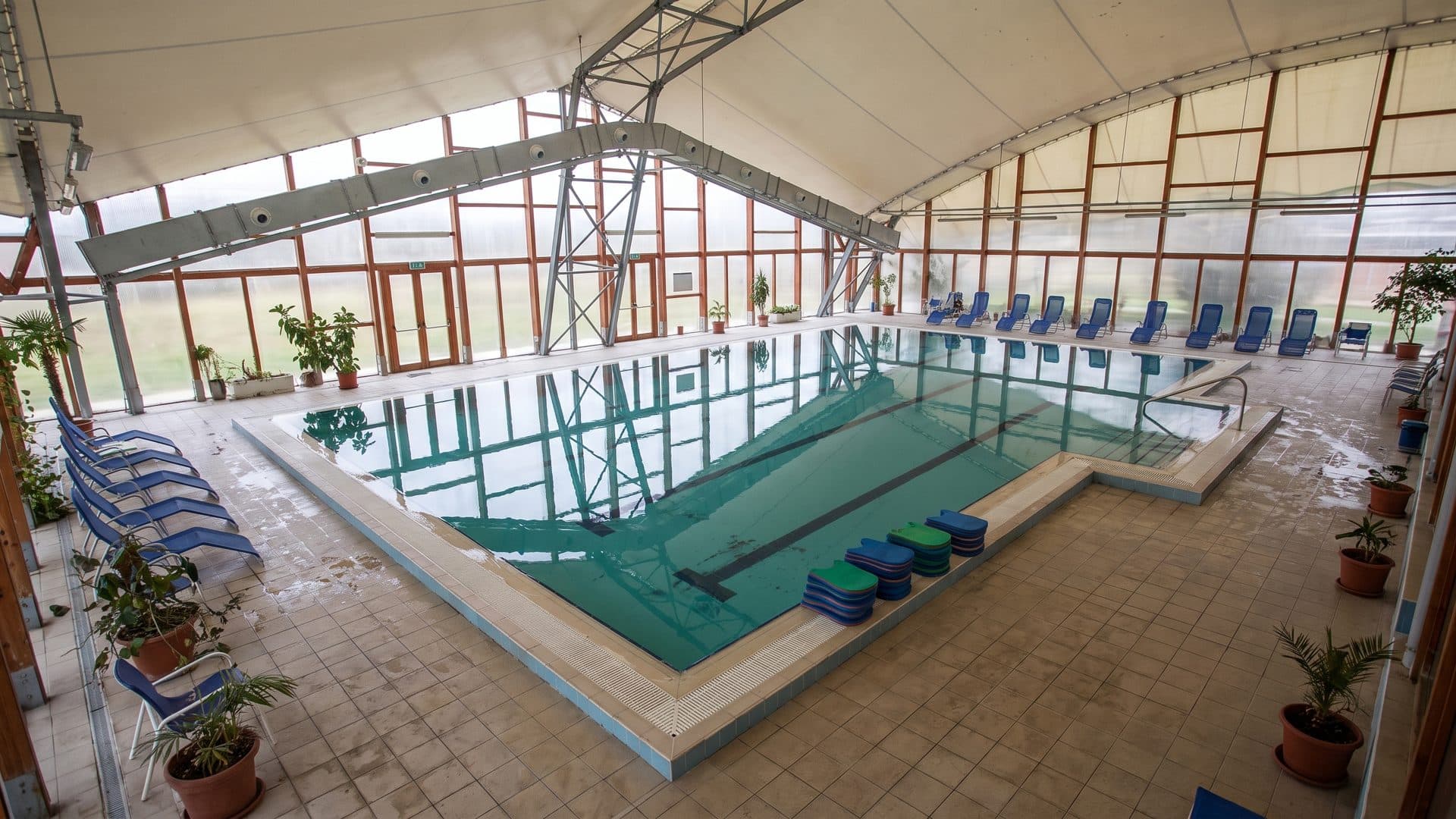 The indoor thermal pool at Akacliget under its glazed timber-framed hall, with loungers along the poolside
