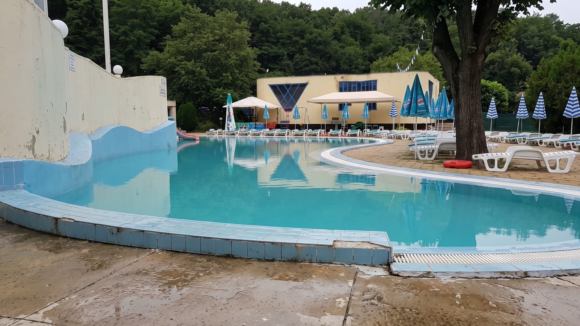 The curving outdoor pool of the Korali water park in Pancharevo with a white wave wall and blue parasols