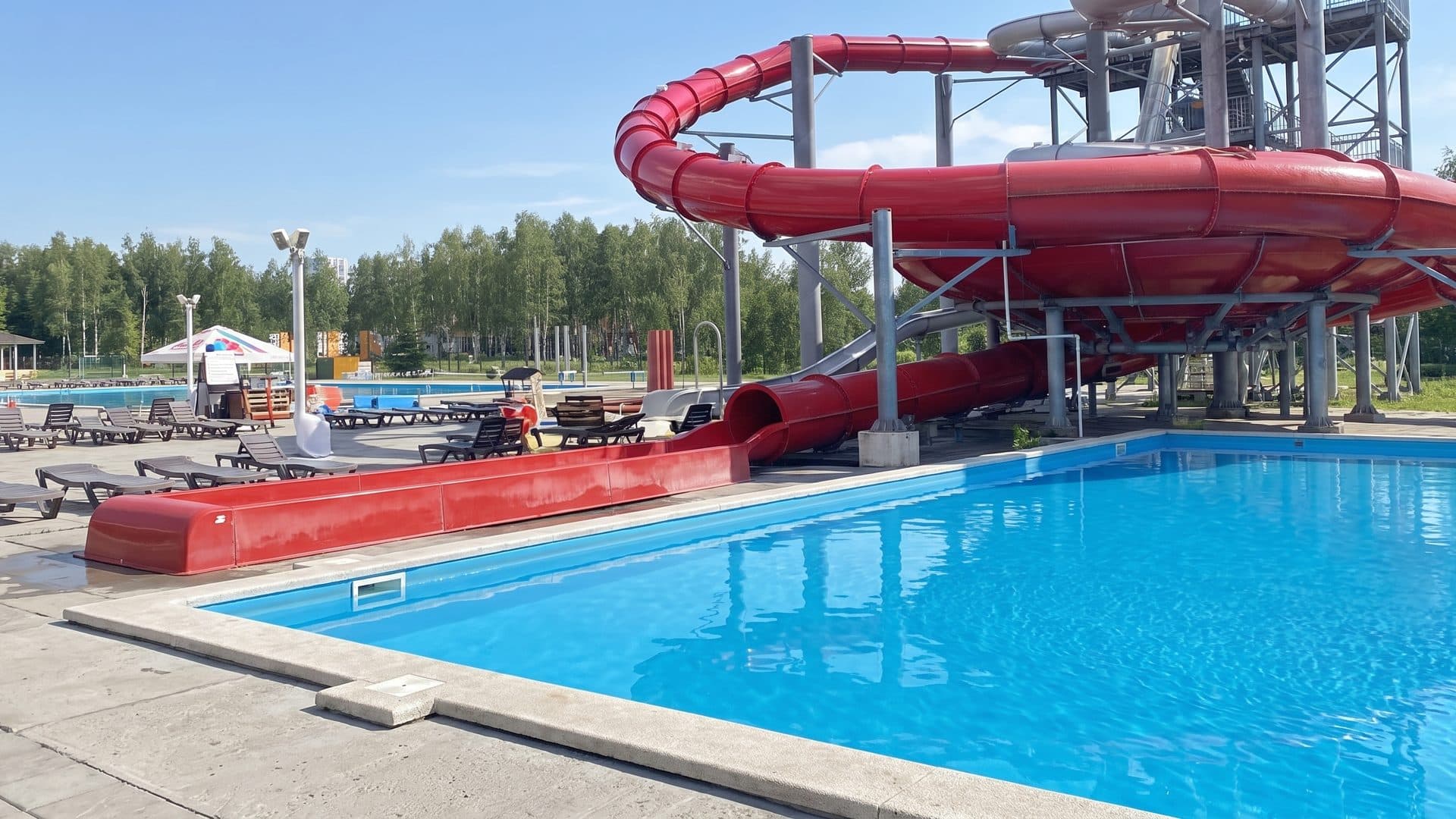 The open-air pool of the Lyabyazhy water park below its red slide among the birches