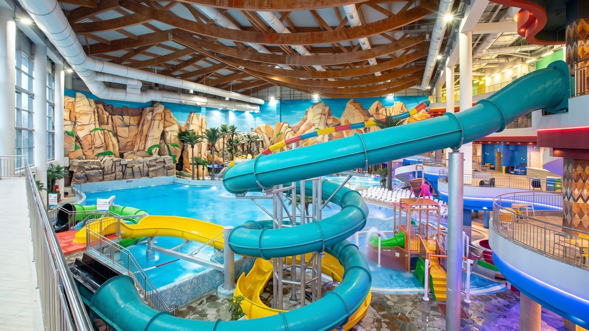 Turquoise and yellow slides over the pools of the Moreon water park, painted rock walls around