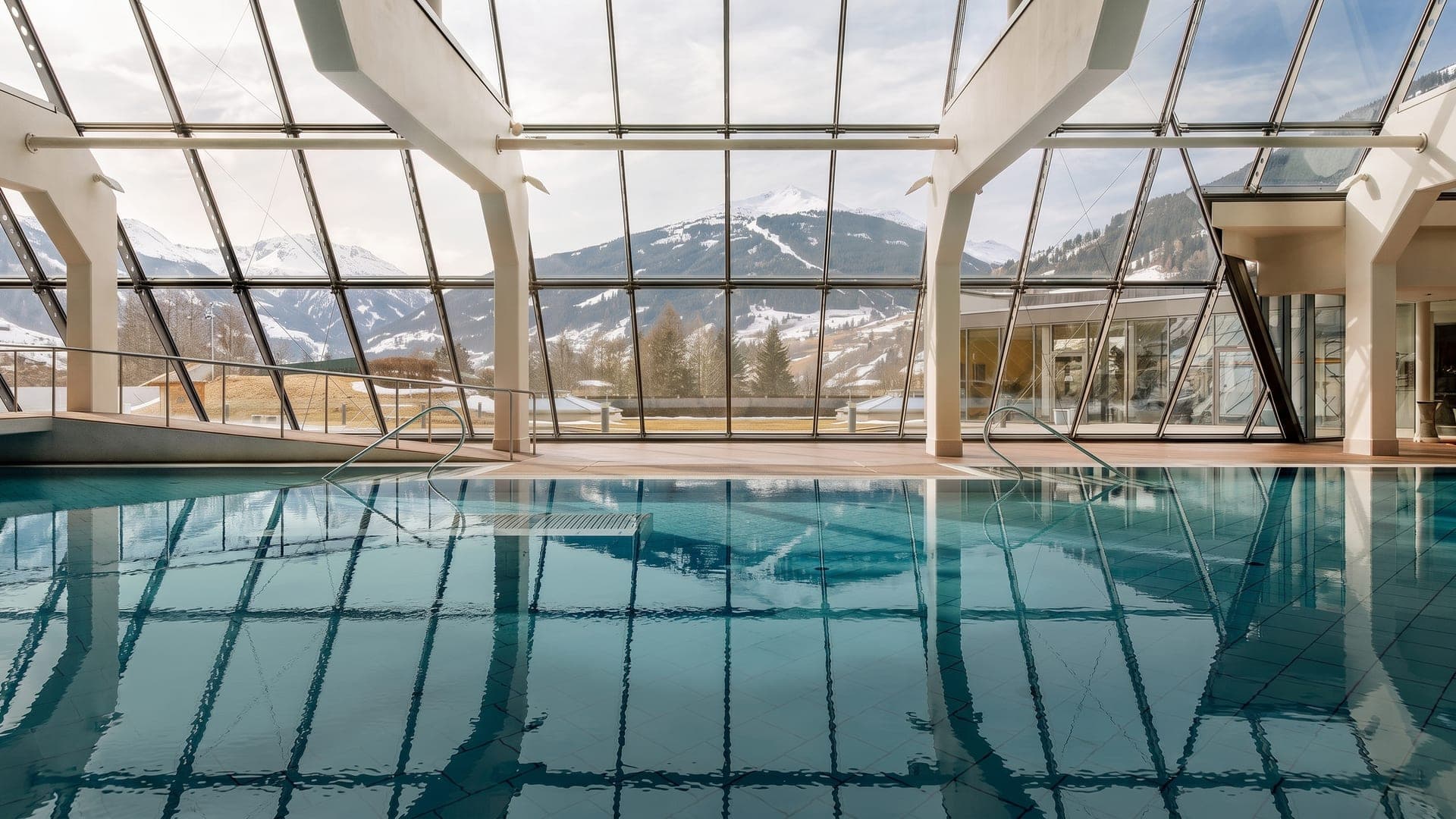 Indoor thermal pool under a glazed roof, with snow-covered mountains visible through the glass