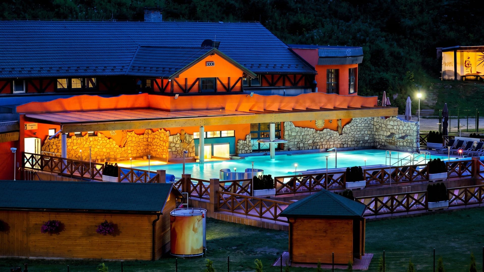 The Aqua Vital Park in Lucky at night, its orange timber buildings lit above the outdoor pool.