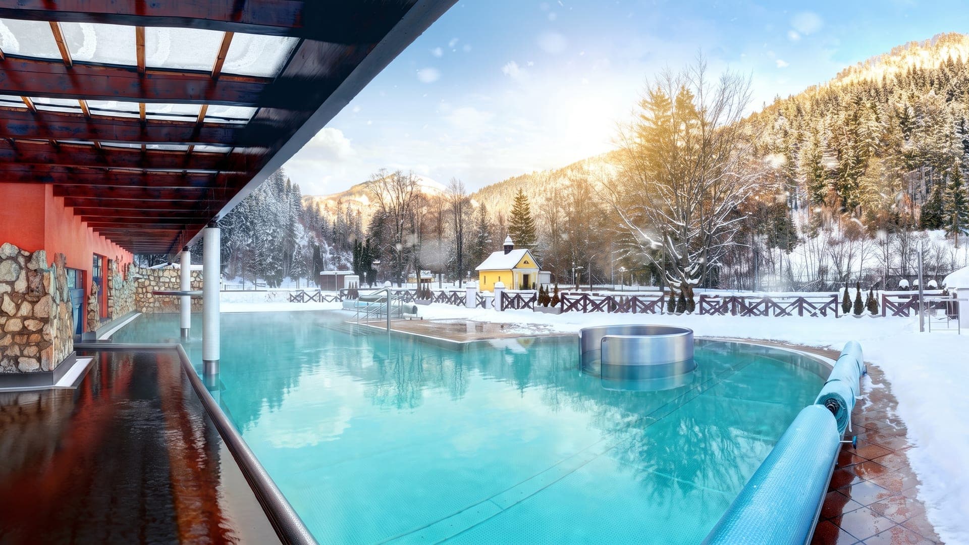 The outdoor thermal pool at the Aqua Vital Park in Lucky in winter, with snow-covered wooded hills behind.