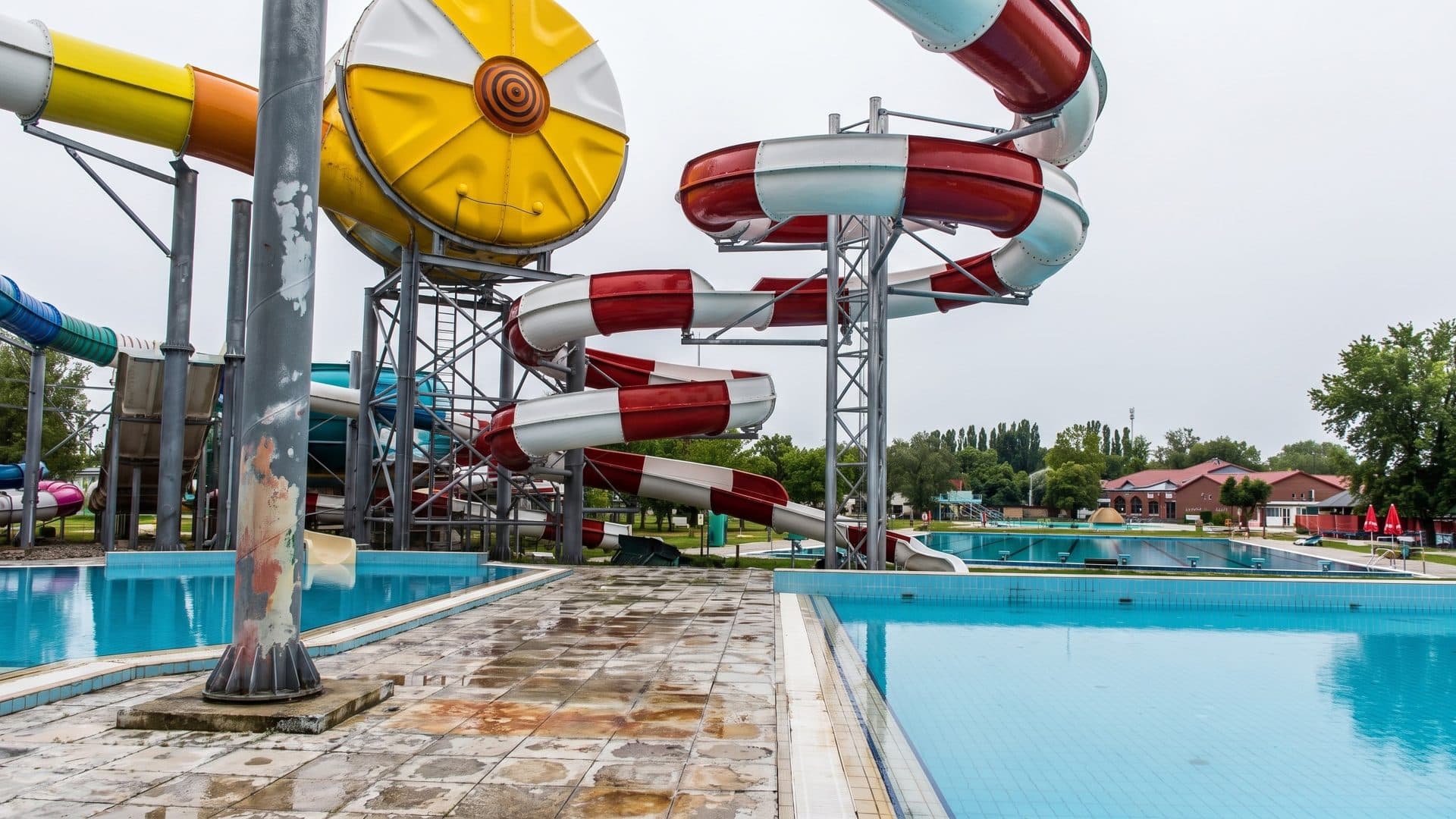 Outdoor pools beneath a cluster of red-and-white spiral waterslides and a large yellow wheel-shaped slide tower