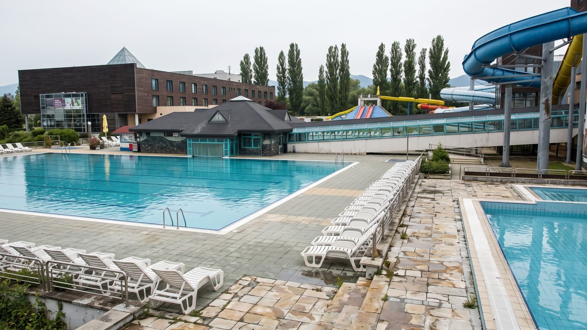 The outdoor pool of AquaCity Poprad with loungers, the dark pavilion and slide tubes behind
