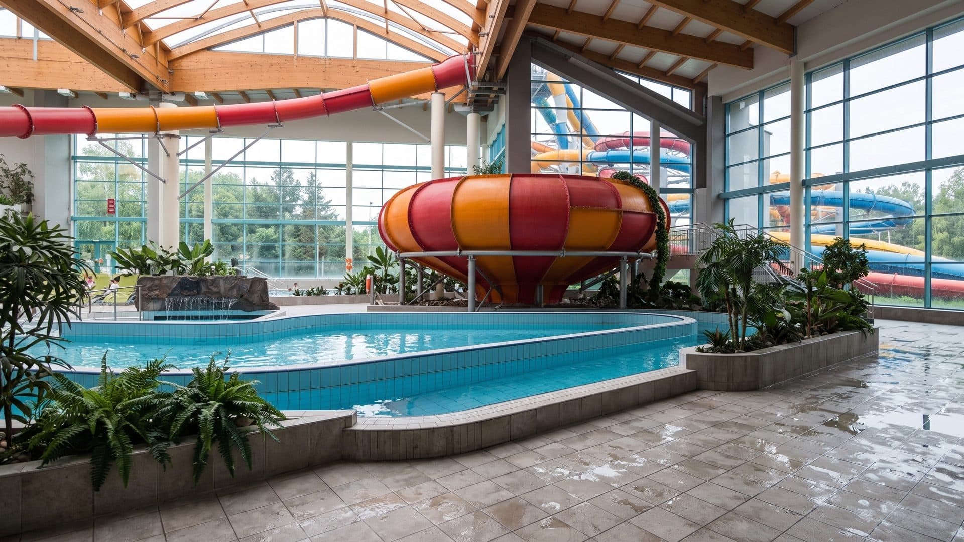 The indoor pool of the Aquadrom in Ruda Slaska with a red and orange bowl slide among planting