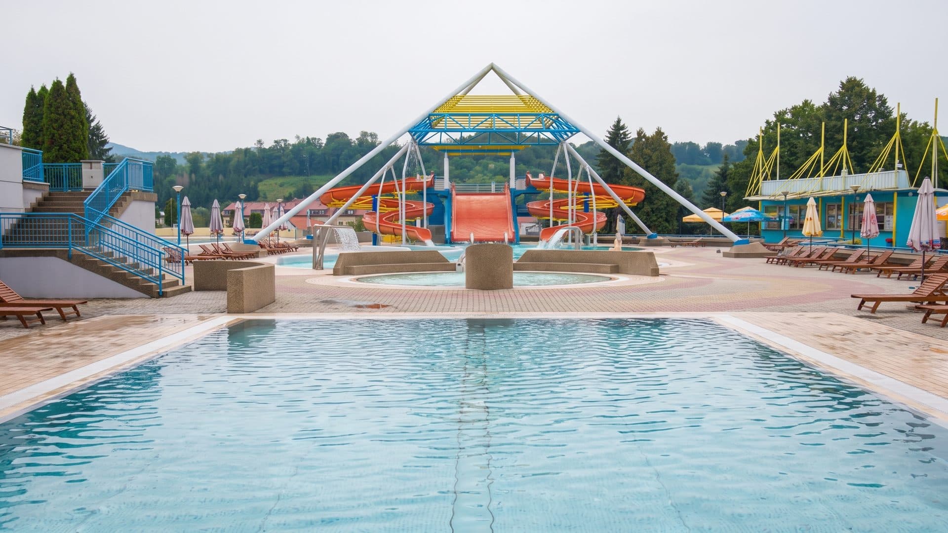 The outdoor pool at Aquae Iasae in Varazdinske Toplice, full and blue, with the painted slide tower rising behind it and loungers along the deck