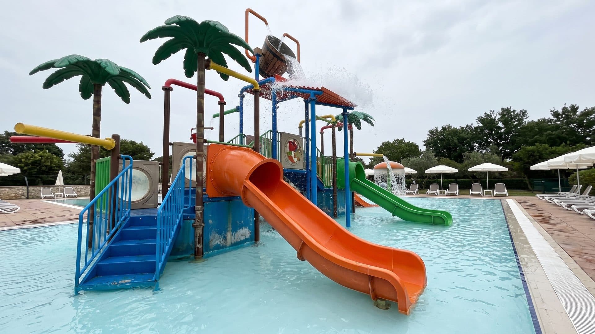 Children's pool with a colourful play structure of slides, ladders and palm-tree water sprayers