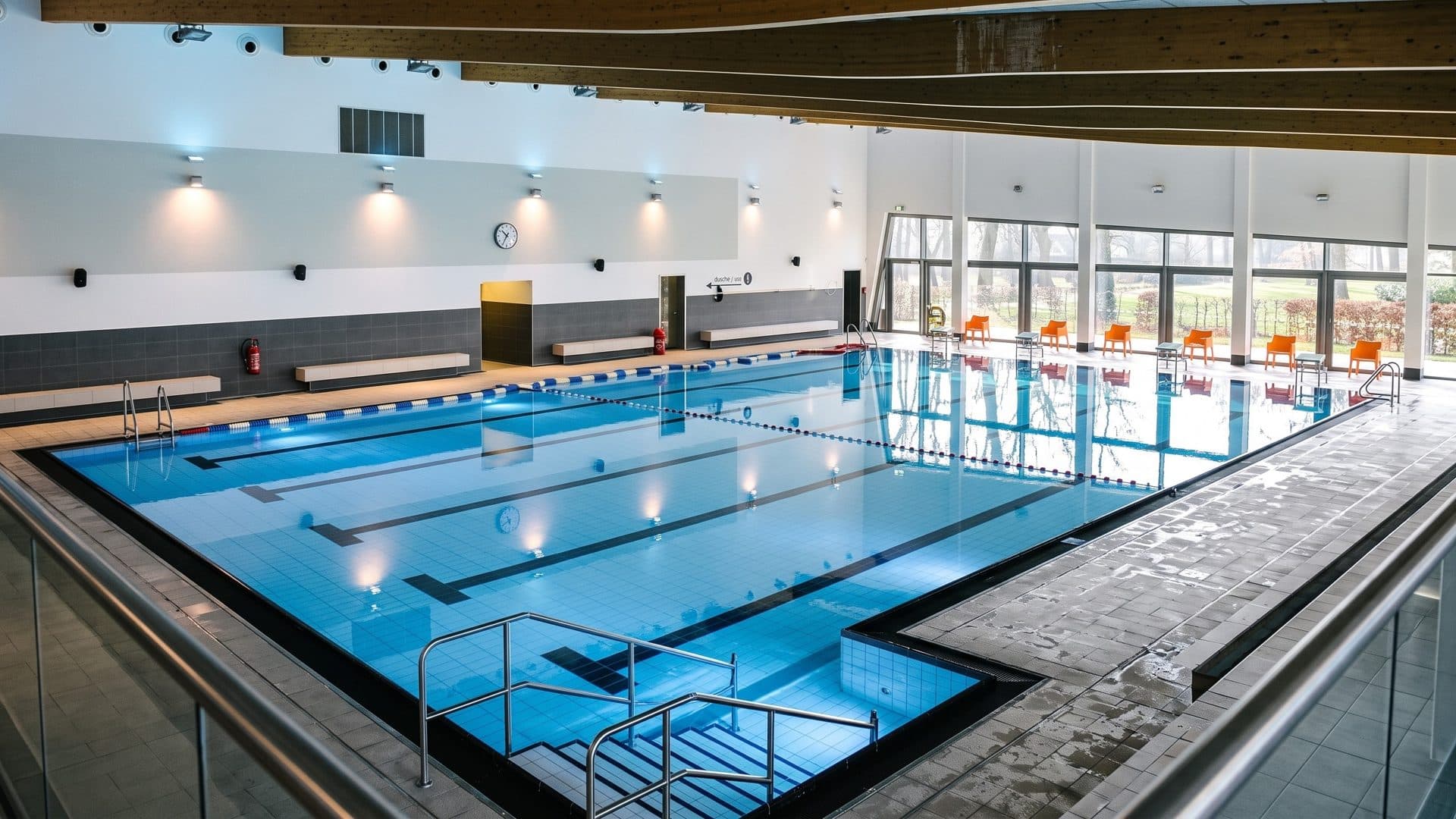 The lane pool of the aquaferrum in Friesoythe with a stepped shallow corner, orange chairs along the glass wall and wall lights above