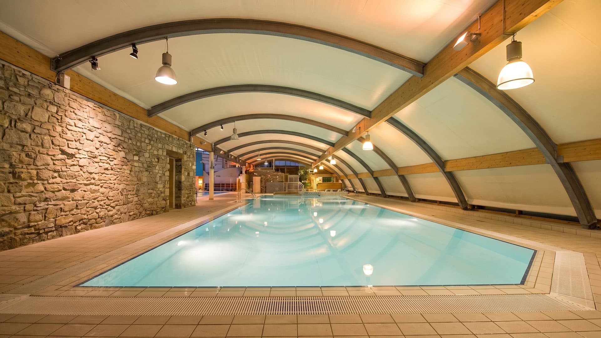 The pool of aquaLaatzium beside its stone wall under the curved tented roof