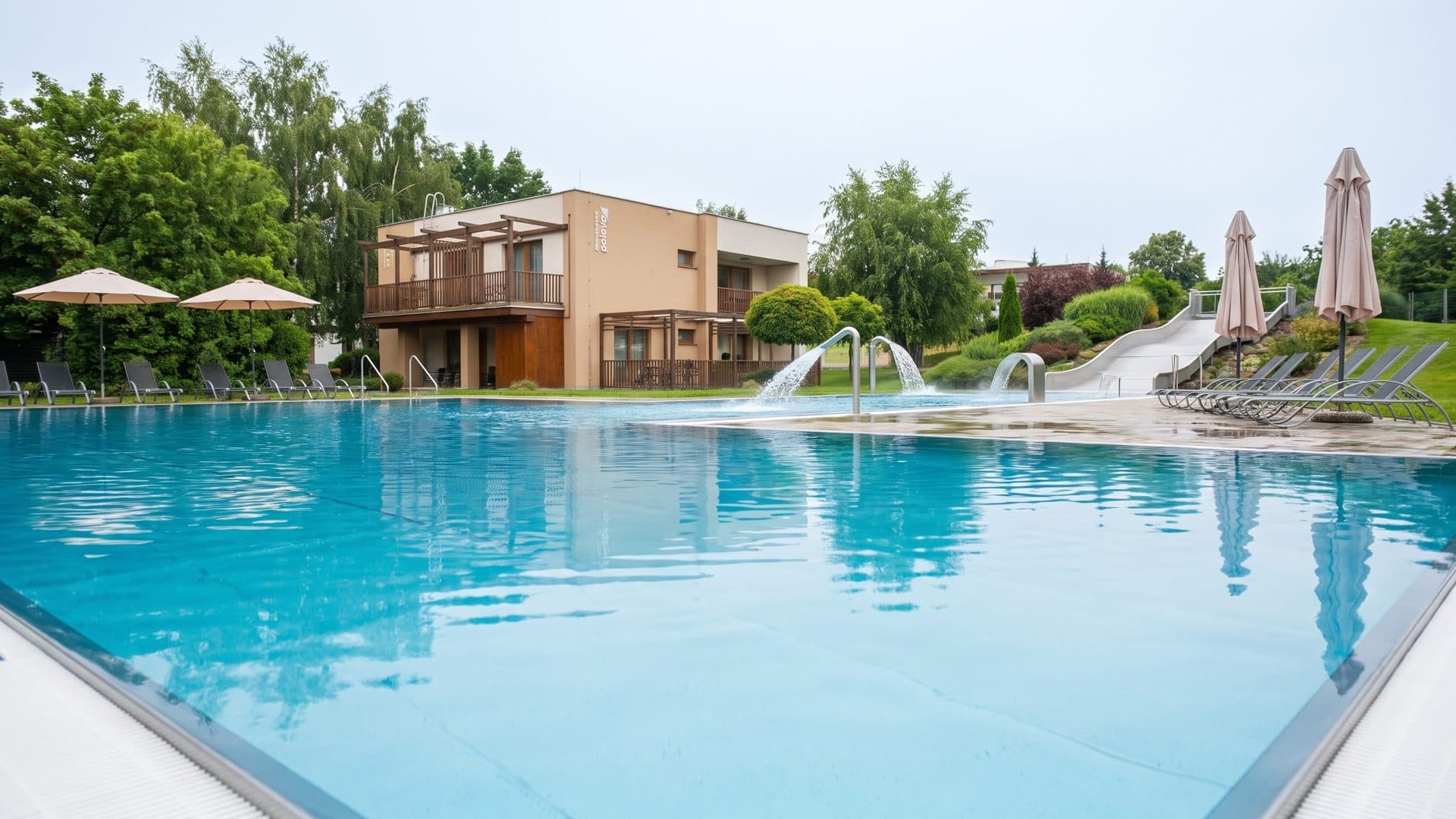 The outdoor pool at Aqualand Moravia with white slides and the resort buildings behind it, parasols along the far edge