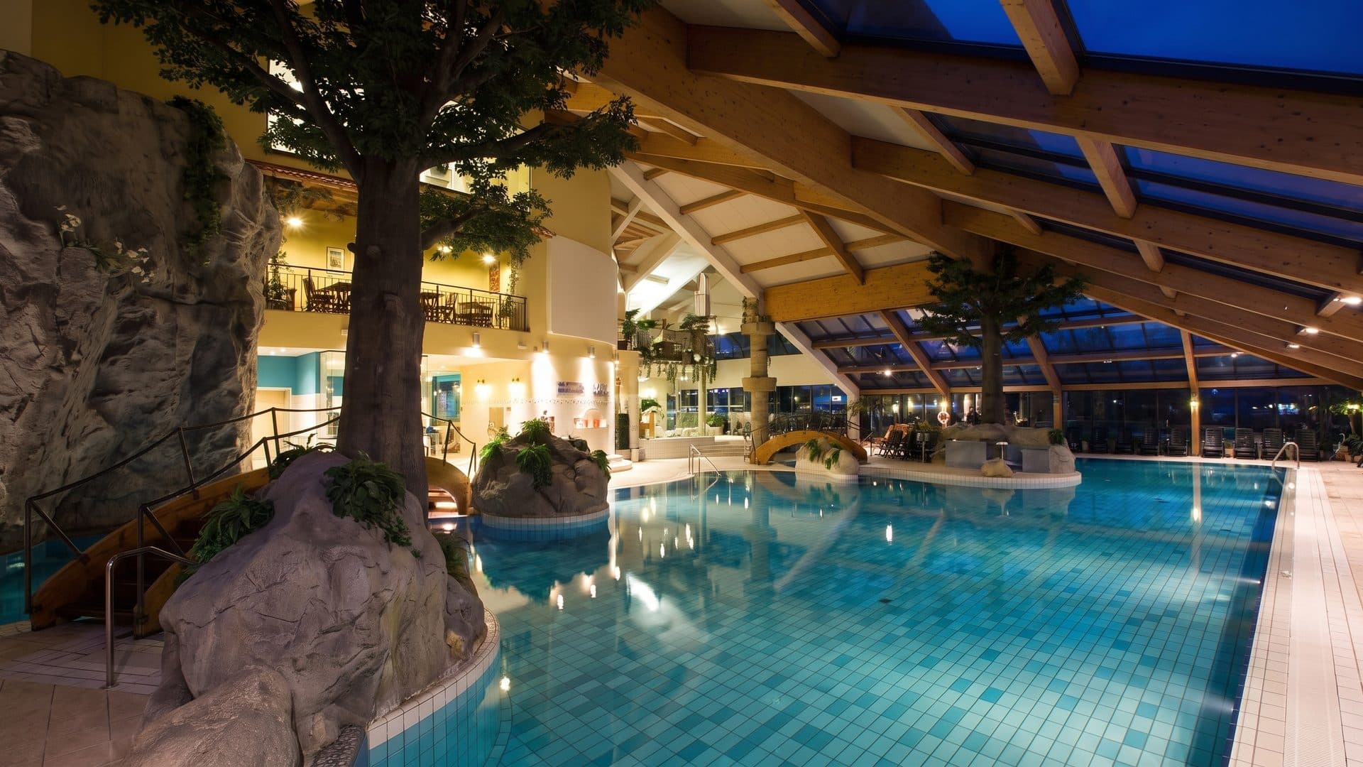 The indoor pool of the Bohinj water park with its rock feature and trees under a timber roof