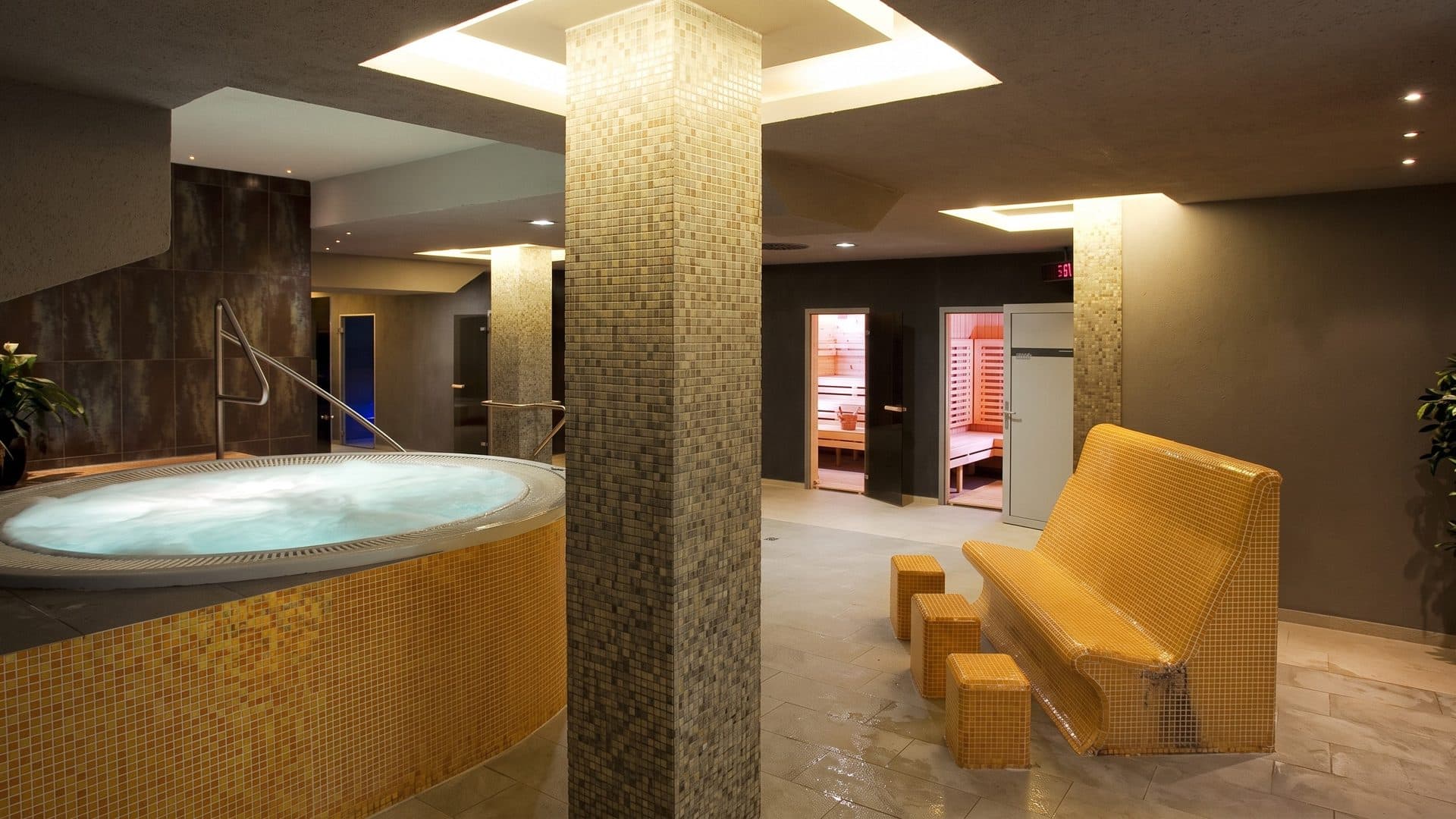 A round tiled whirlpool at Aquapark Delna in Presov beside a mosaic column and sauna doors