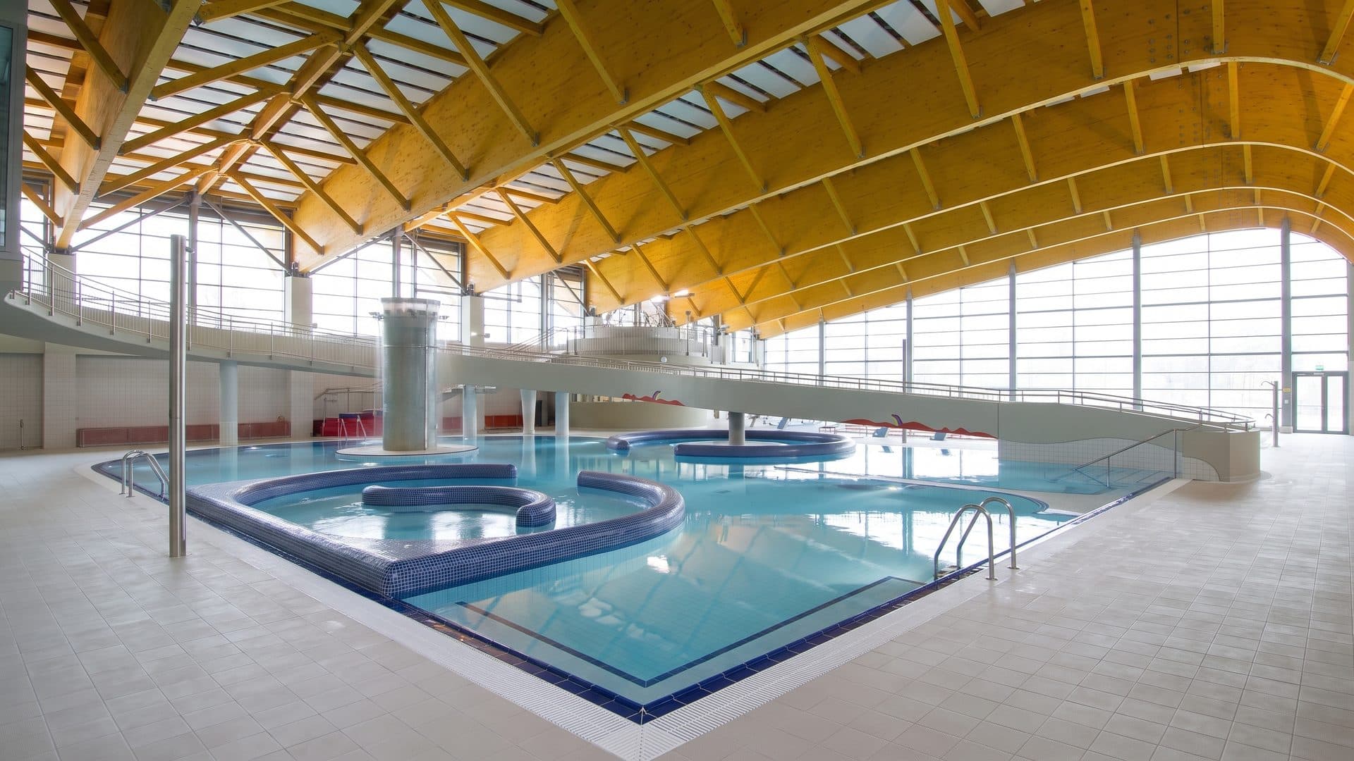 The hall of the Kohoutovice water park with its yellow roof trusses above the pools