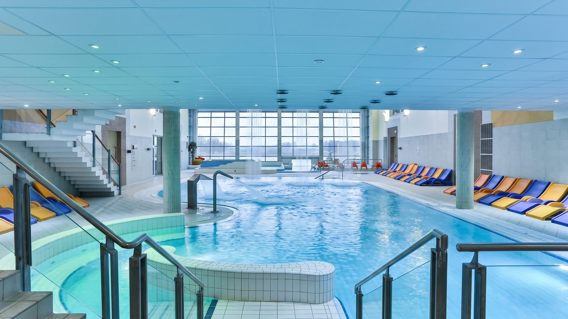 The indoor thermal pool of Aquapark Senec with steps, handrails and yellow and blue loungers