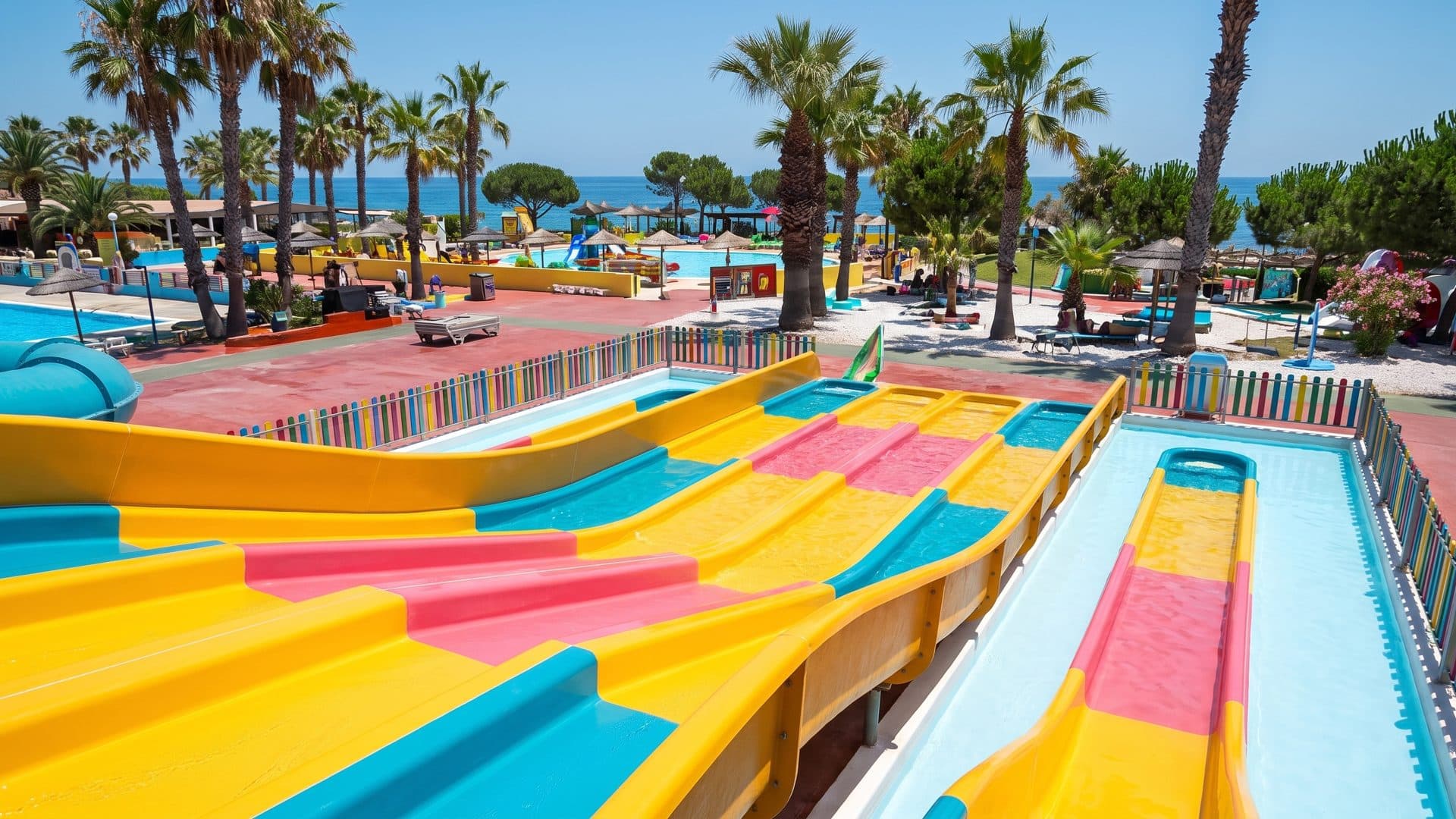 The multi-lane racer slide of Aquatropic running down between the palms above the sea