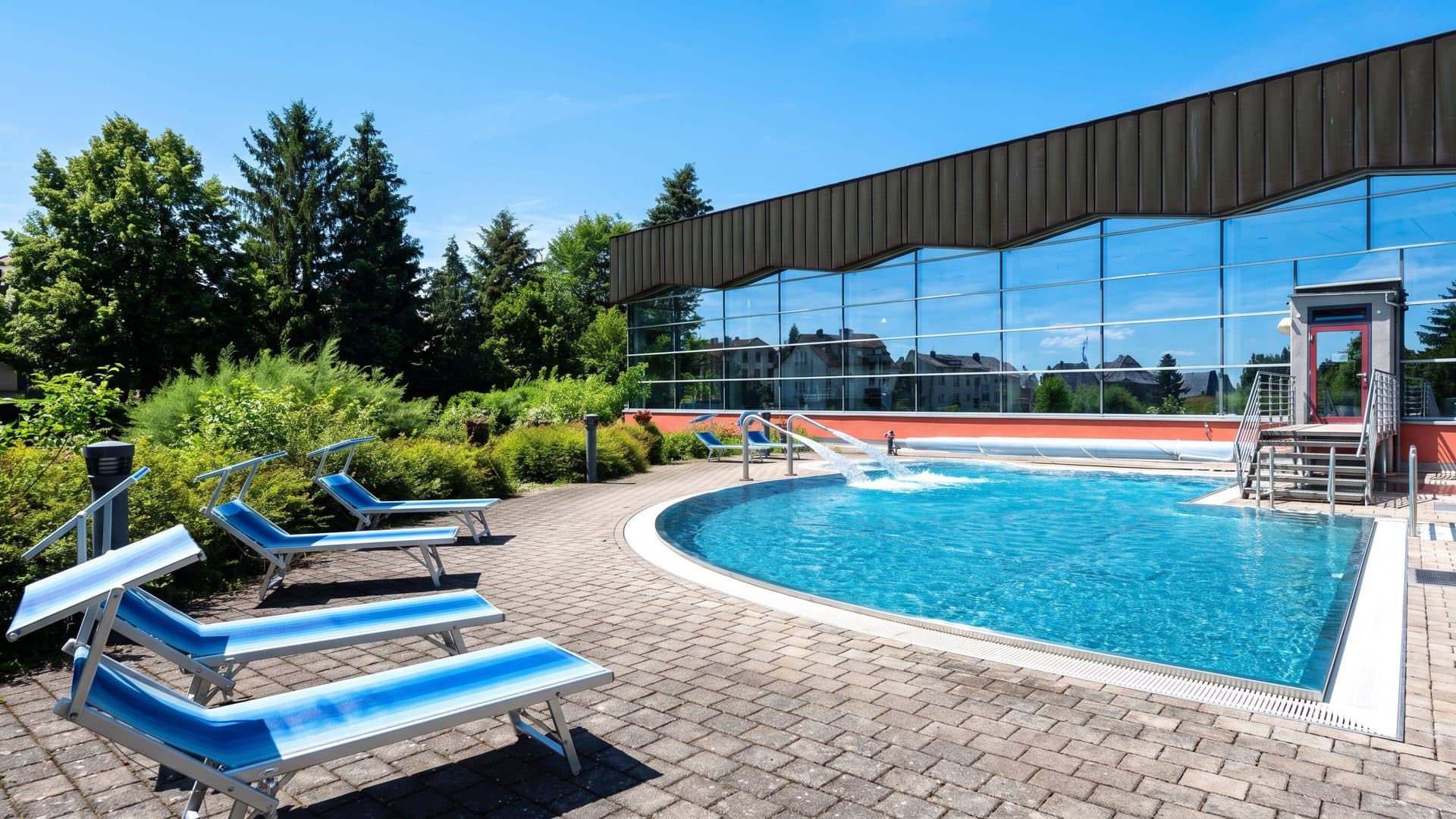 The outdoor pool of the Aquawell along its loungers beside the glazed bath building