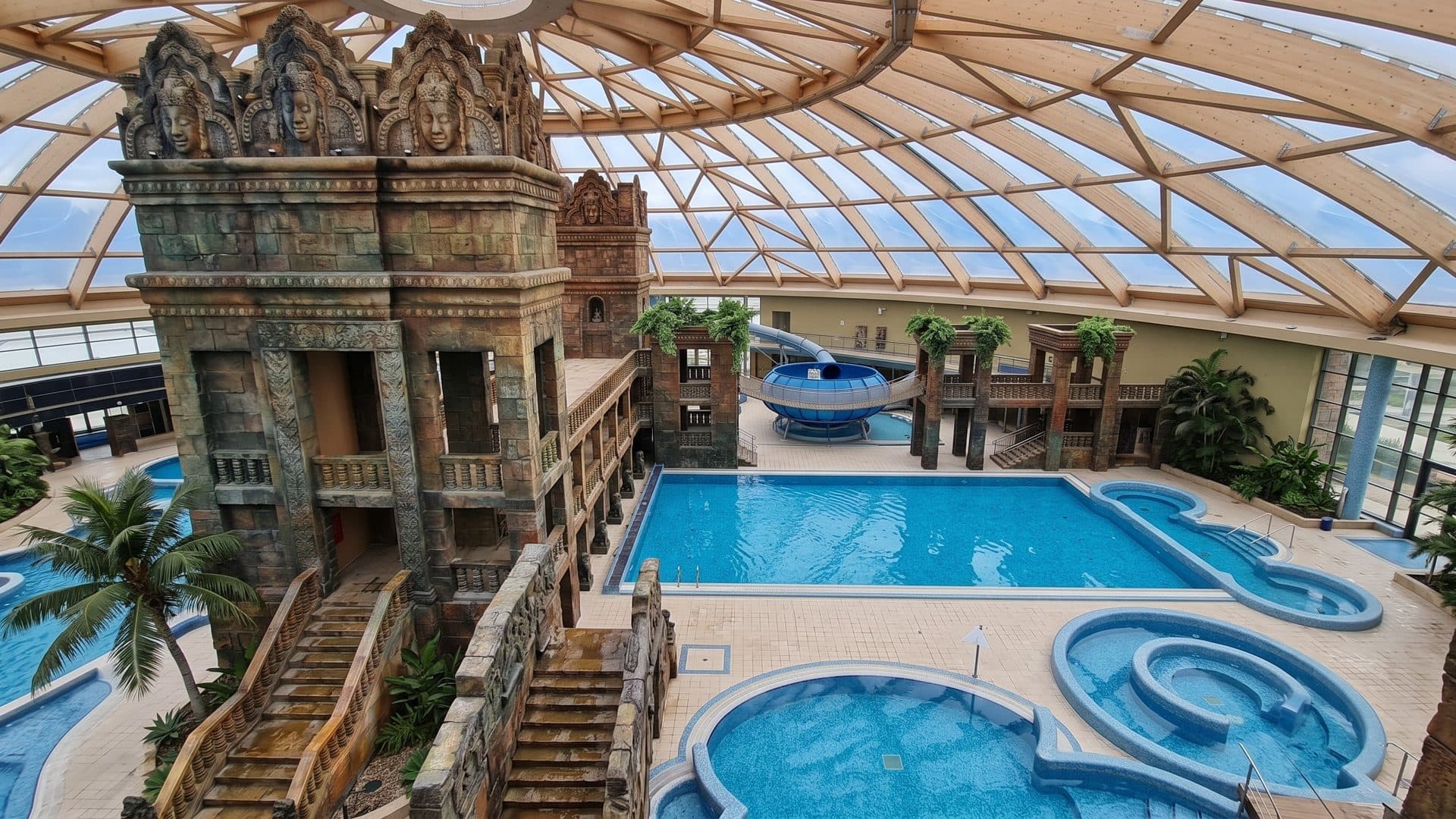 Pools of Aquaworld Budapest below the carved temple towers under a large timber-ribbed glass dome