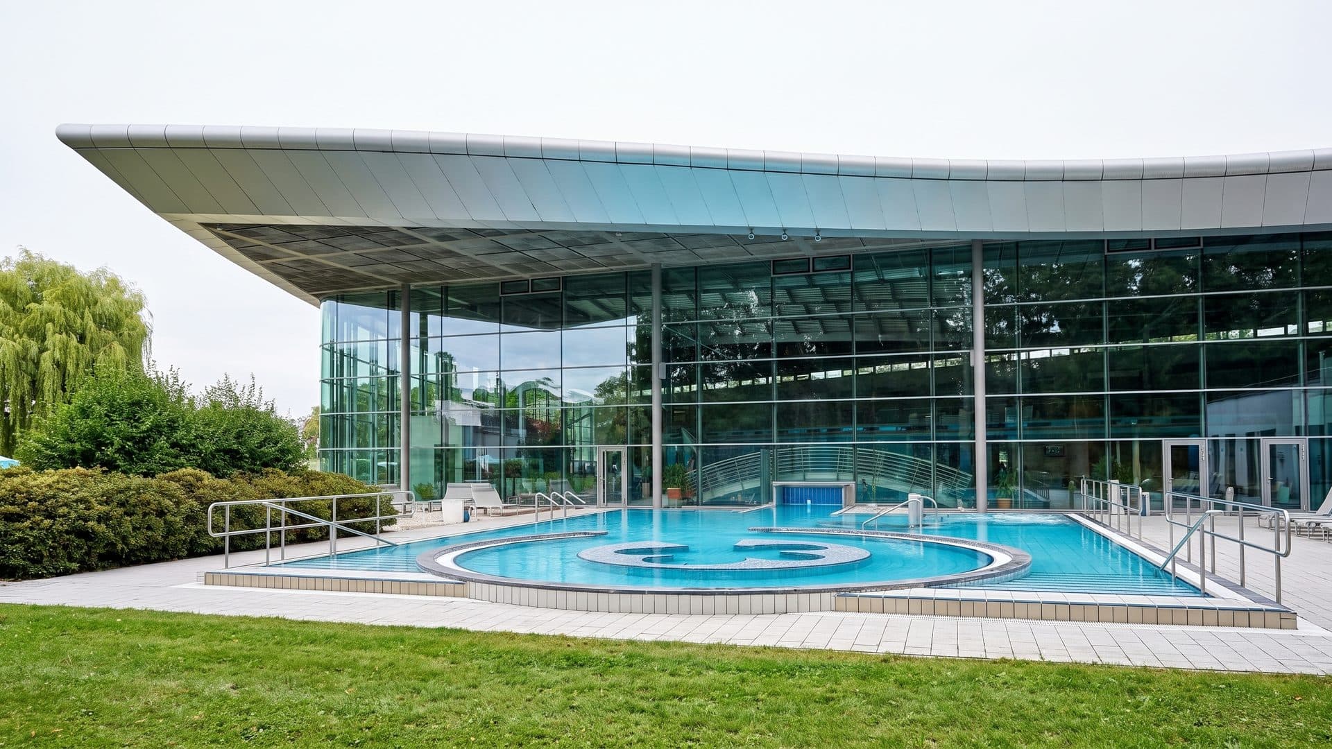 The glazed wave of the Ardesia-Therme building with its outdoor pool in front
