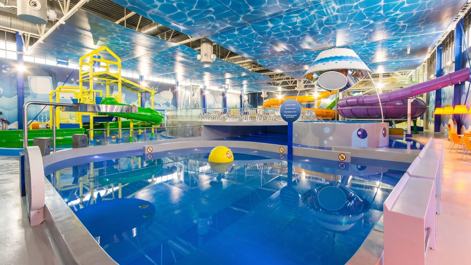 The indoor hall of Atlantis H2O at Viimsi, a blue-lit pool in the foreground and the coloured slide structures rising behind it