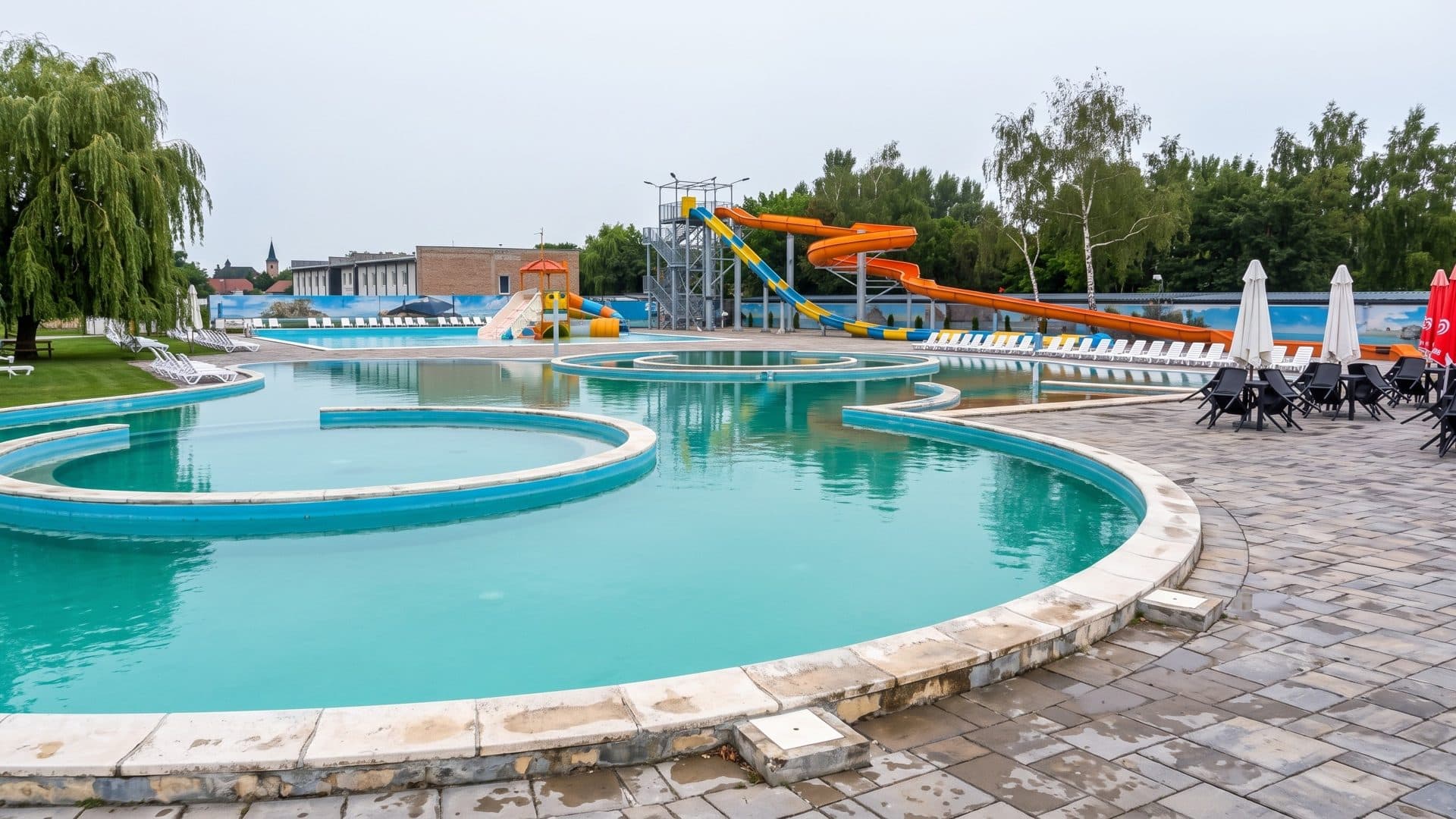 Curved outdoor thermal pools of the AVA Thermalpark in Diakovce, with the slide tower and loungers beyond