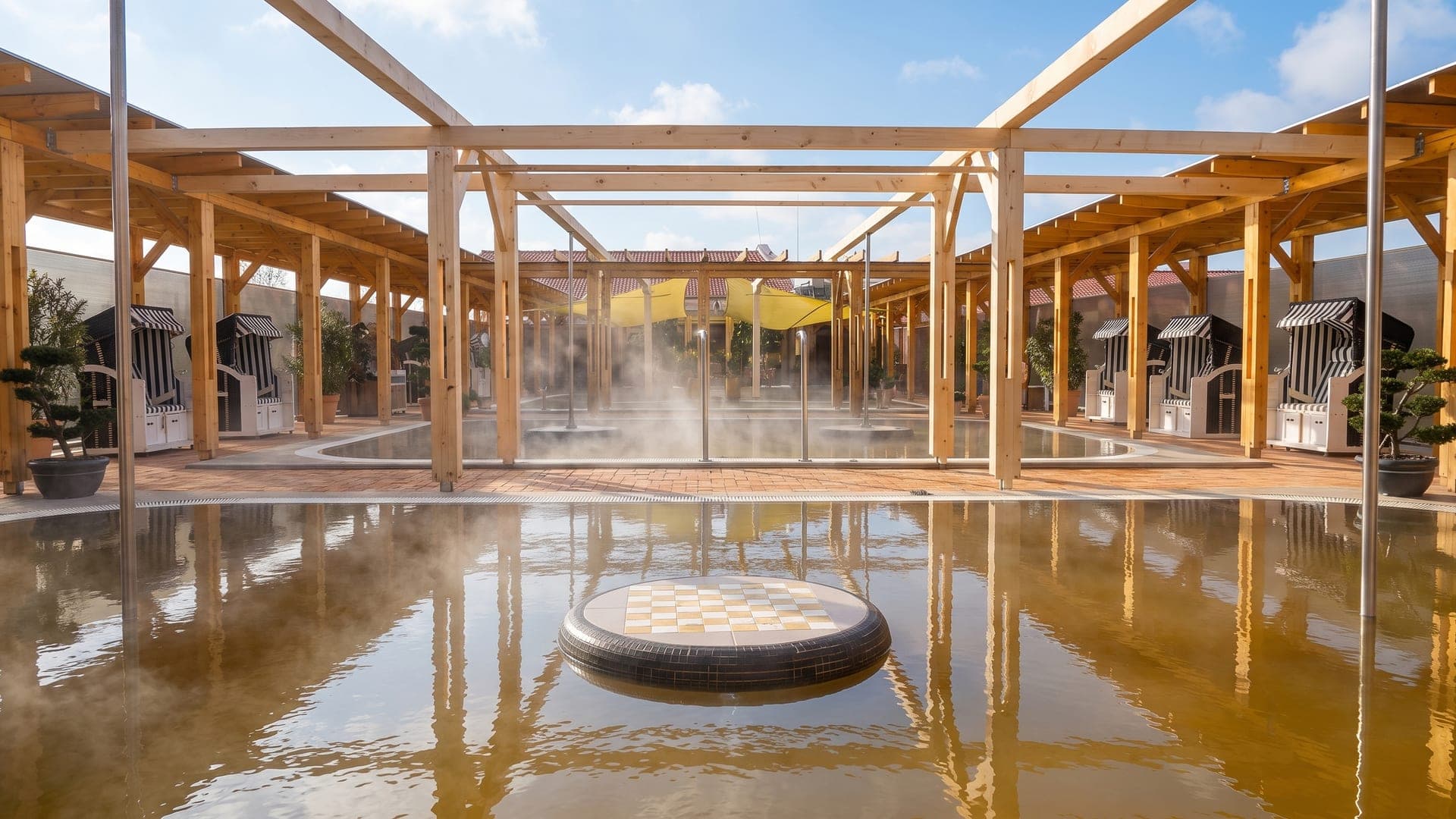 Steaming pool under a timber pergola, ringed by hooded wicker beach chairs
