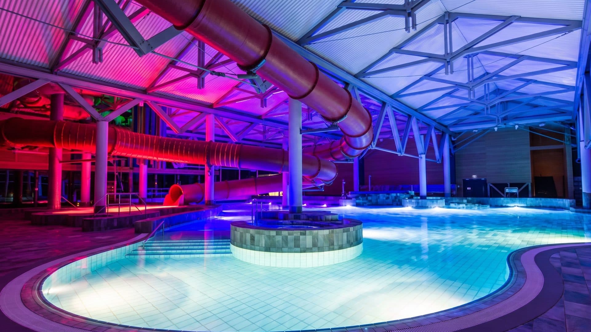 The pool hall of the bade:haus under its slide tubes in pink and blue light