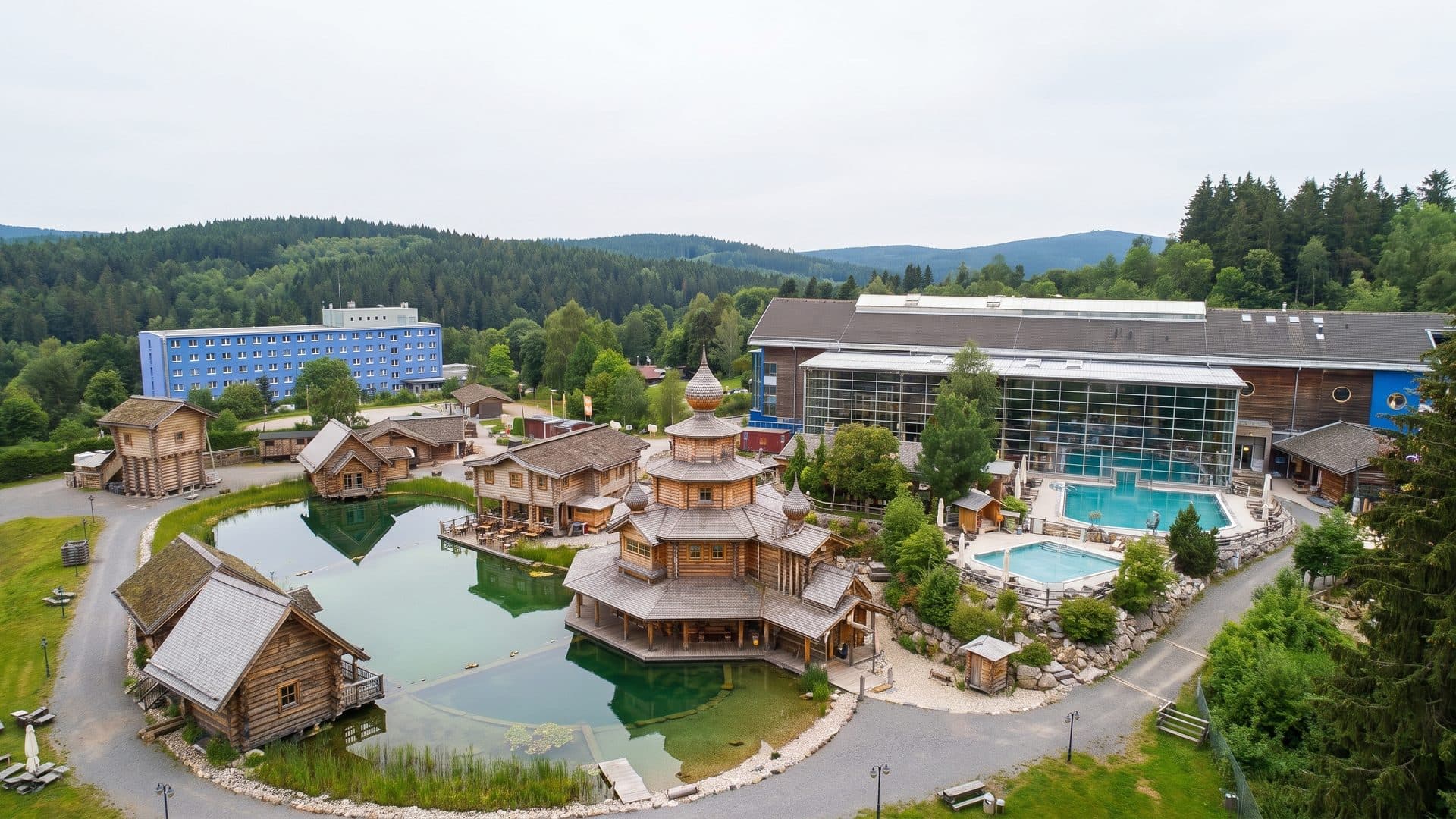 The Badegaerten Eibenstock seen from the air: timber buildings and pools among wooded hills