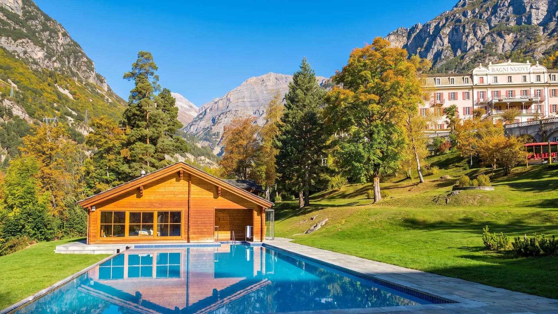 The pink facade of the Bagni Nuovi above Bormio in autumn, its pool and timber pavilion on the lawn below.