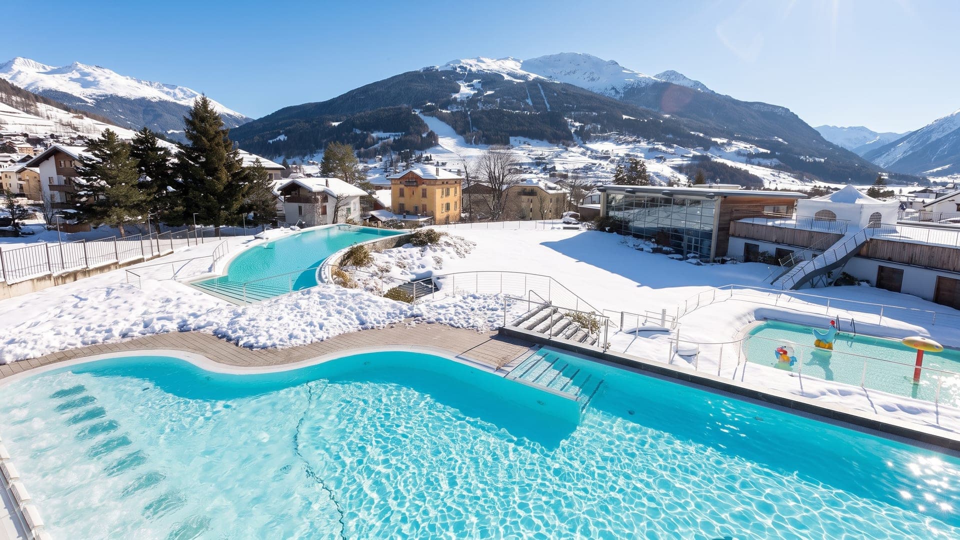 The turquoise outdoor pools of the Bagni Nuovi above Bormio, cut into the snow with the alpine valley beyond.