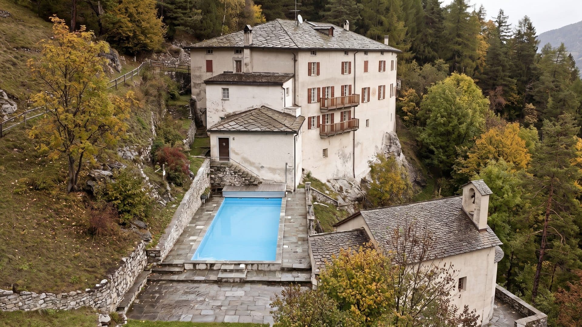 The old stone bathhouse clinging to a wooded mountainside, with a narrow blue pool on the terrace below