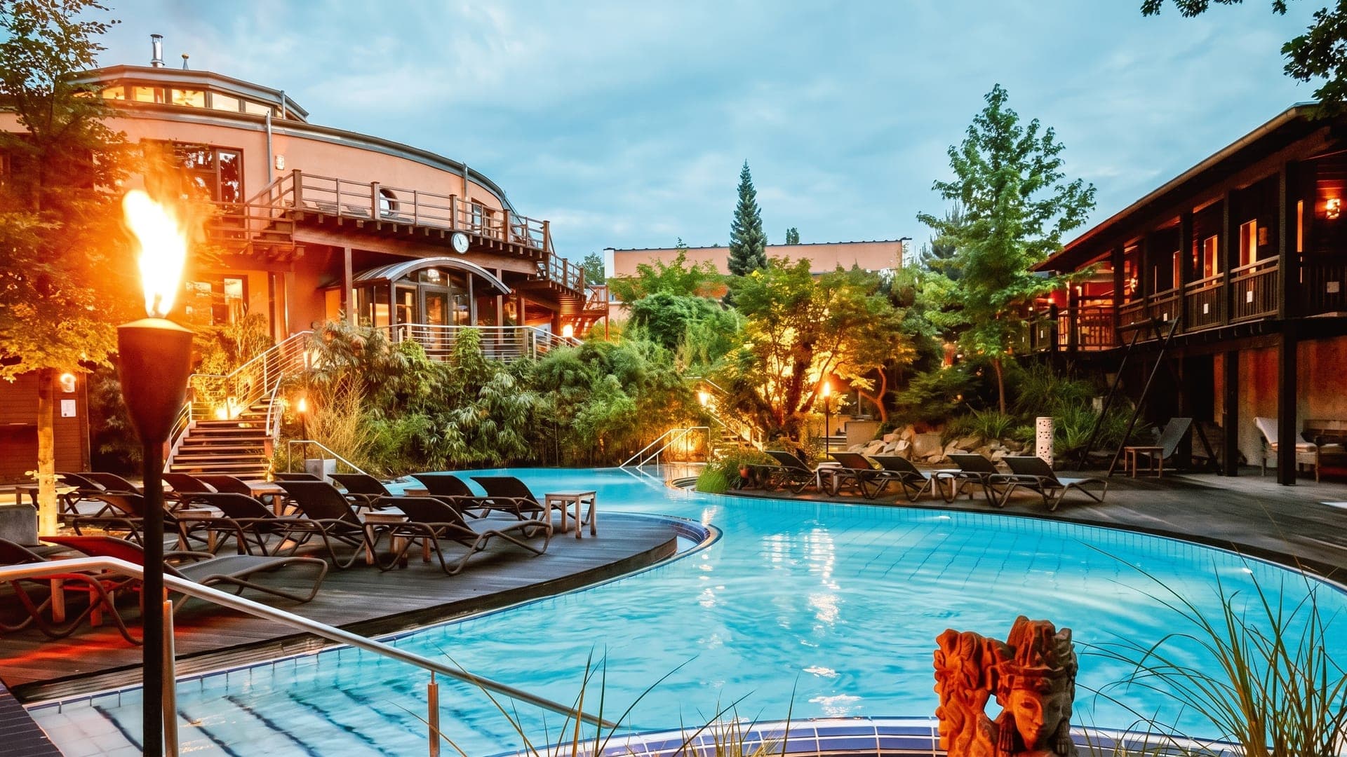 Outdoor pool at dusk with burning torches and timber balconies above