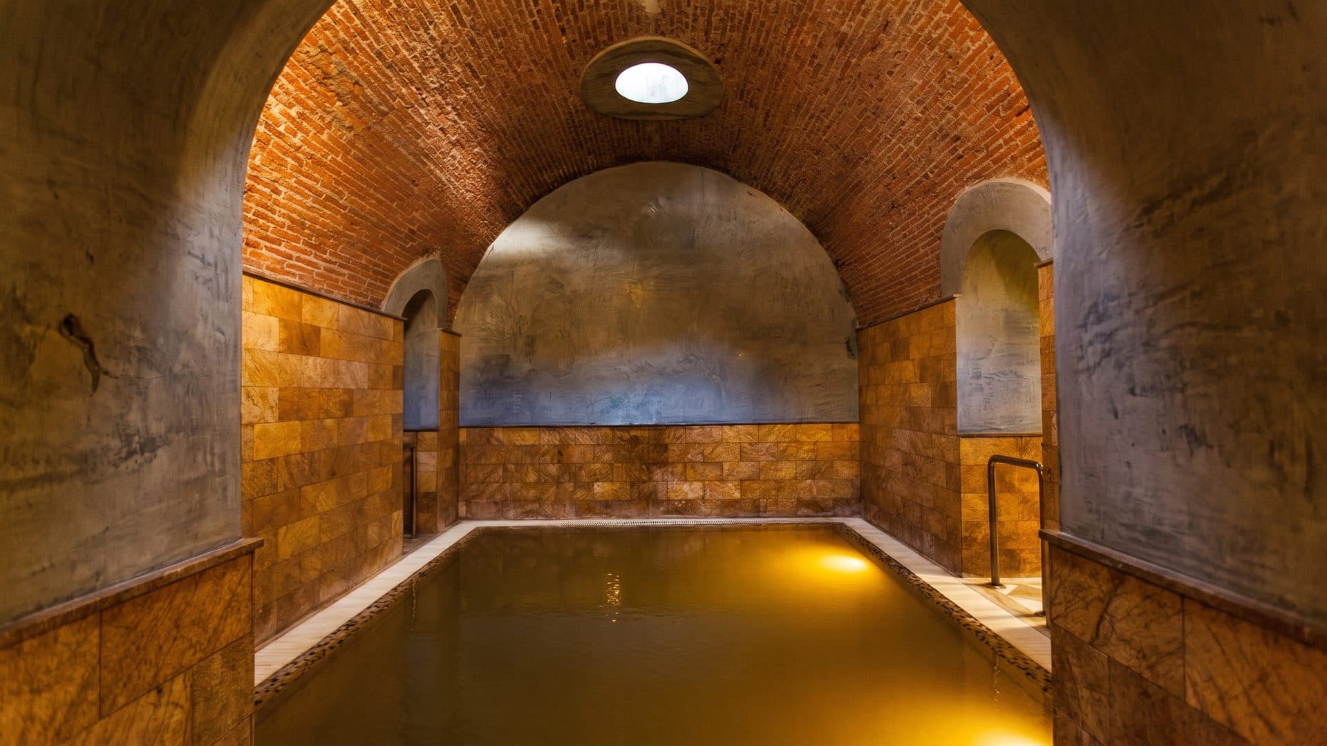 The vaulted thermal bathing chamber at Balneario de Graena: a brick barrel vault with an oculus above the pool.