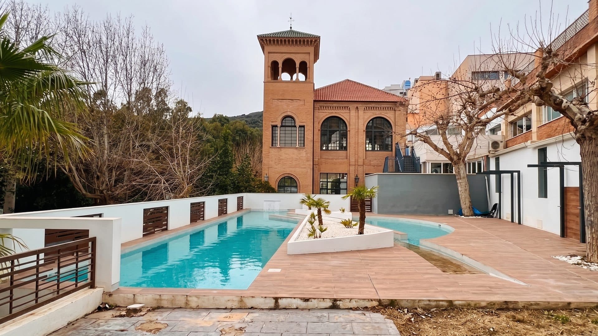 The spa's brick tower and arcaded wing above a turquoise pool in a walled garden.