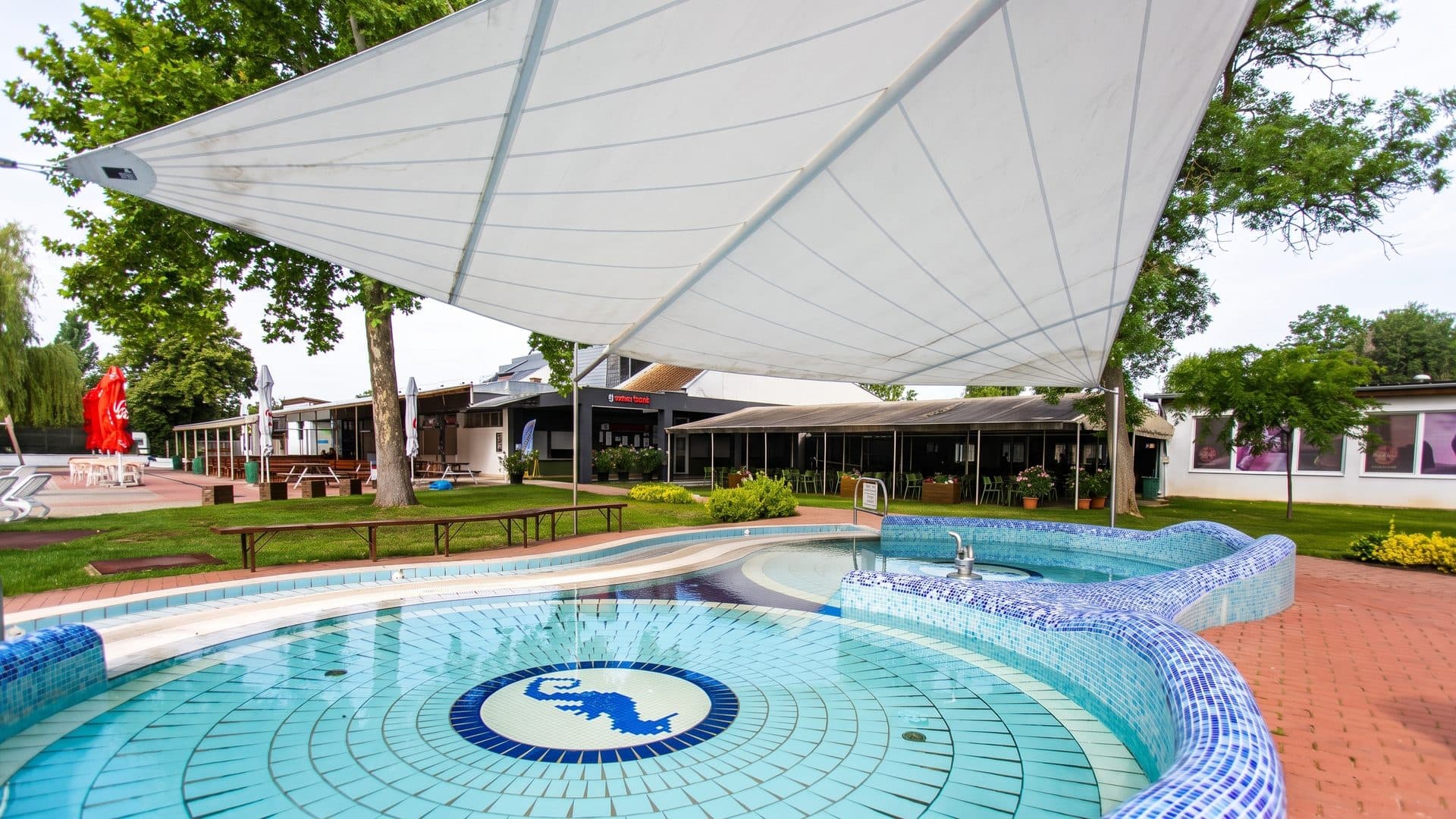 The outdoor mosaic pool of Barack Thermal Resort under its white tensile canopy, lawn and trees behind