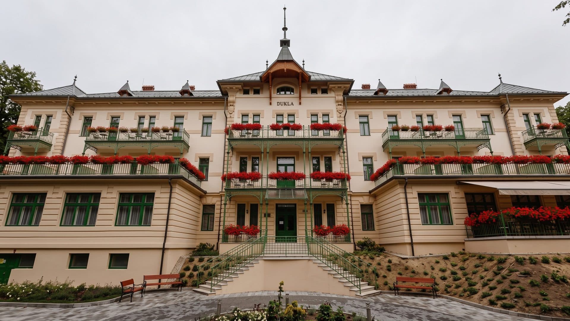 The cream spa house of Bardejovske Kupele with green cast-iron balconies and red geraniums along every floor