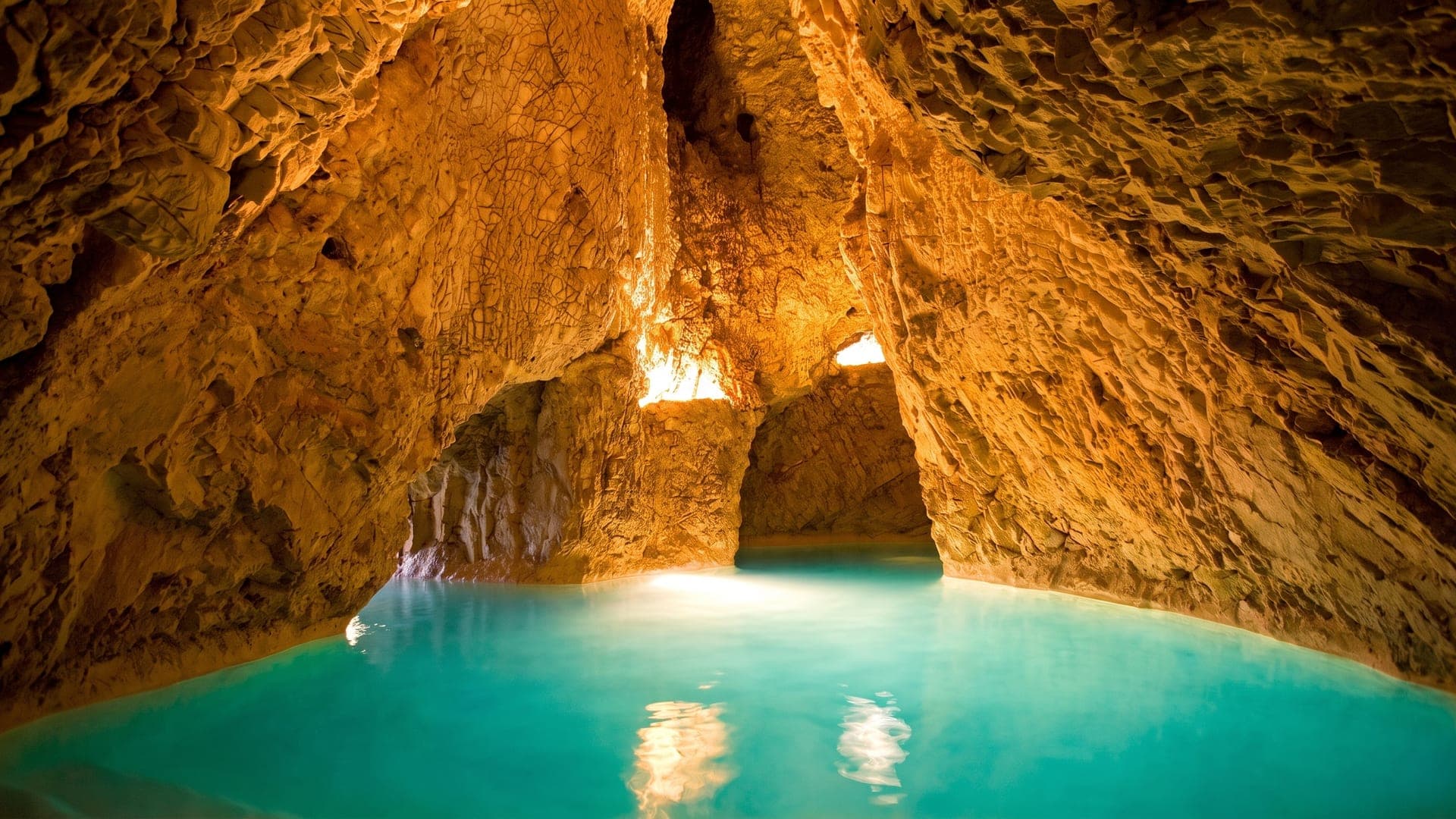 Cave pool of turquoise water beneath lit limestone rock