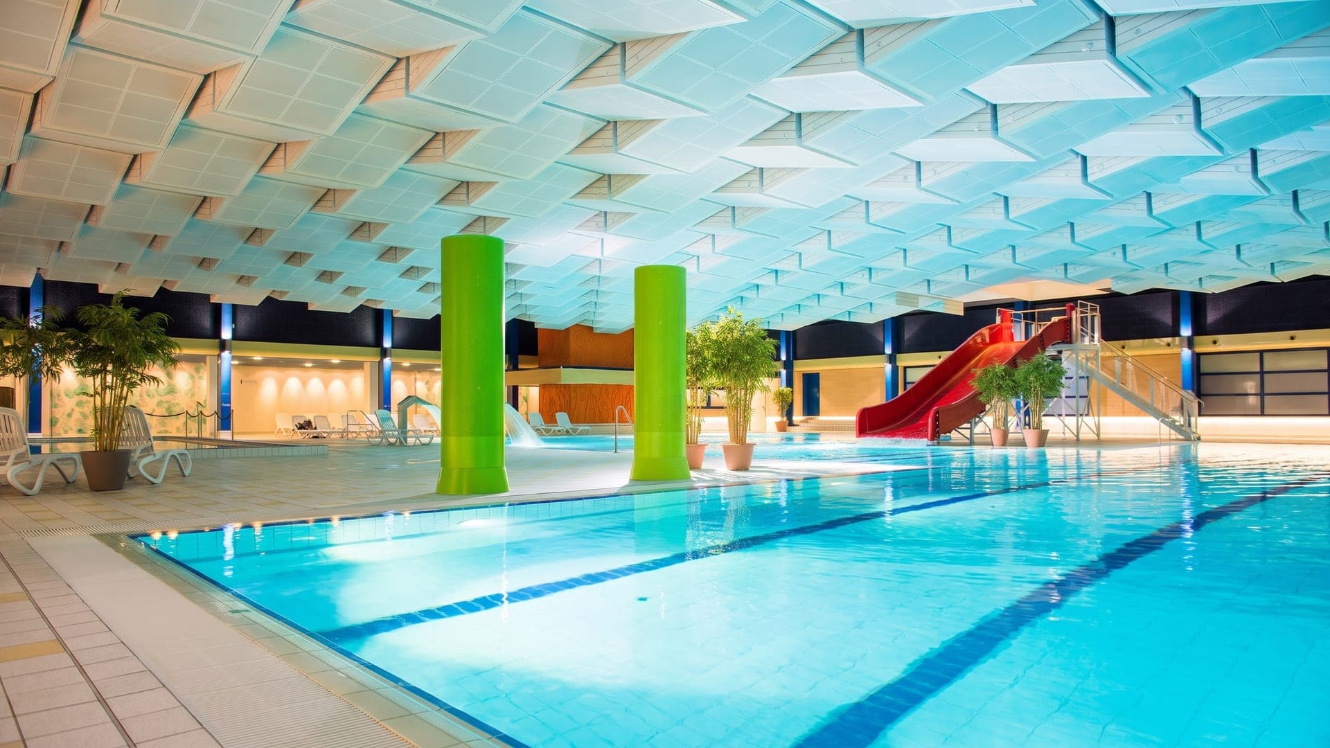 Indoor pool hall with green columns, a red slide and a patterned ceiling