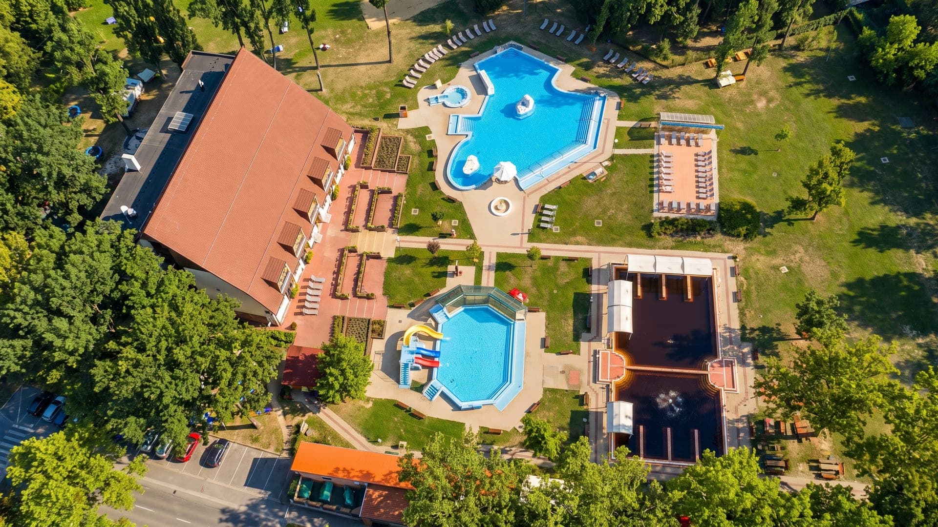 Aerial view of the outdoor pools and a red-roofed building set in green parkland