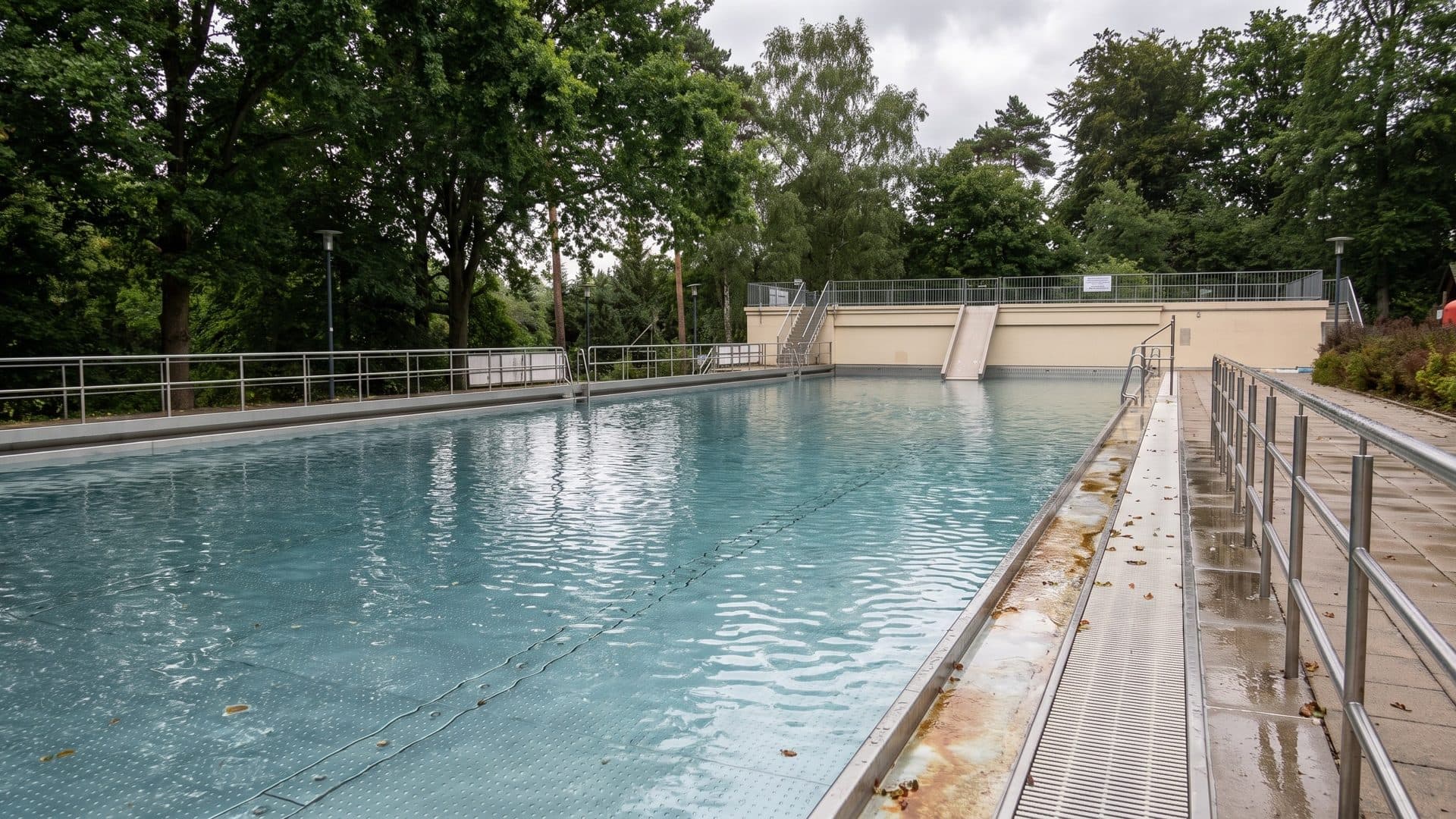 The long historic open-air pool between trees, with a slatted walkway along its edge