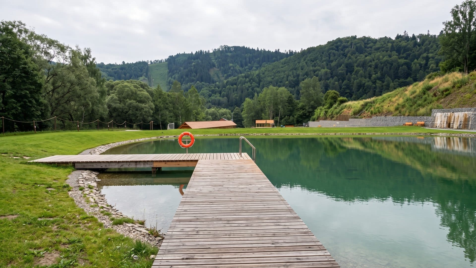 The natural swimming pond of Levocska Dolina with a timber jetty and a lifebuoy, wooded hills behind