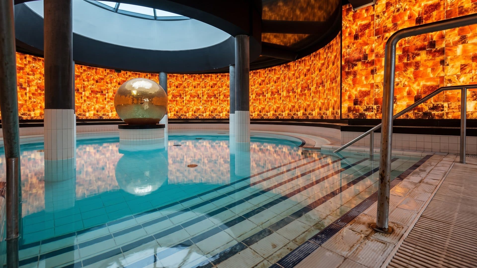 The indoor pool of Bogn Engiadina with a golden sphere, under a round skylight between glowing salt-stone walls