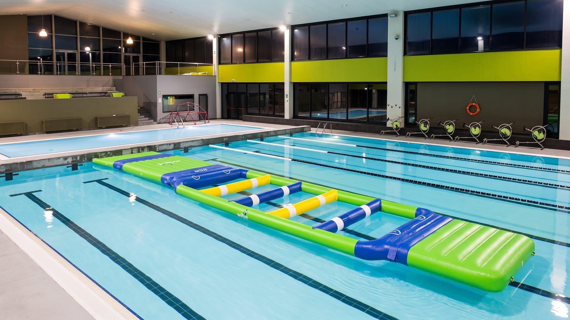 The indoor pool hall at Bormio Terme, with swimming lanes and an inflatable course on the water.
