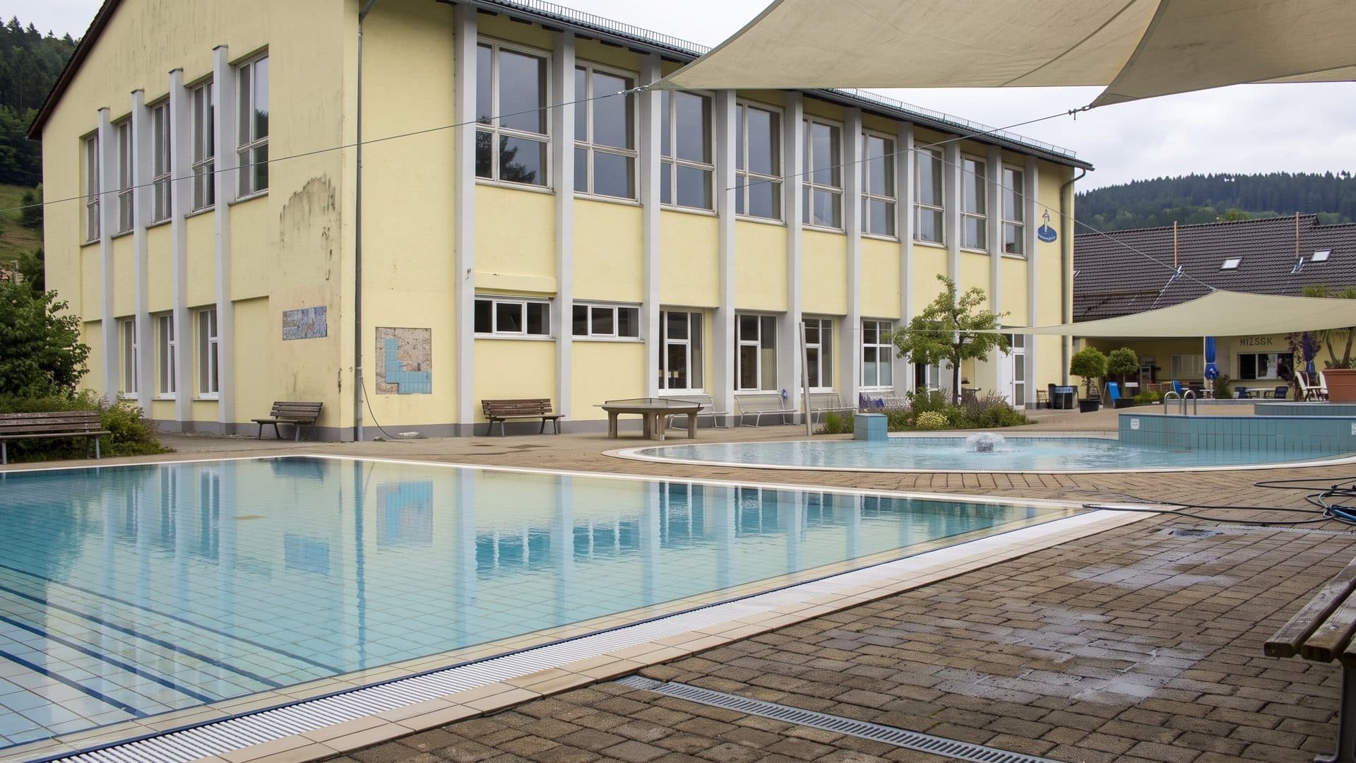 The outdoor pool of the Bregtalbad in front of the yellow school-style building