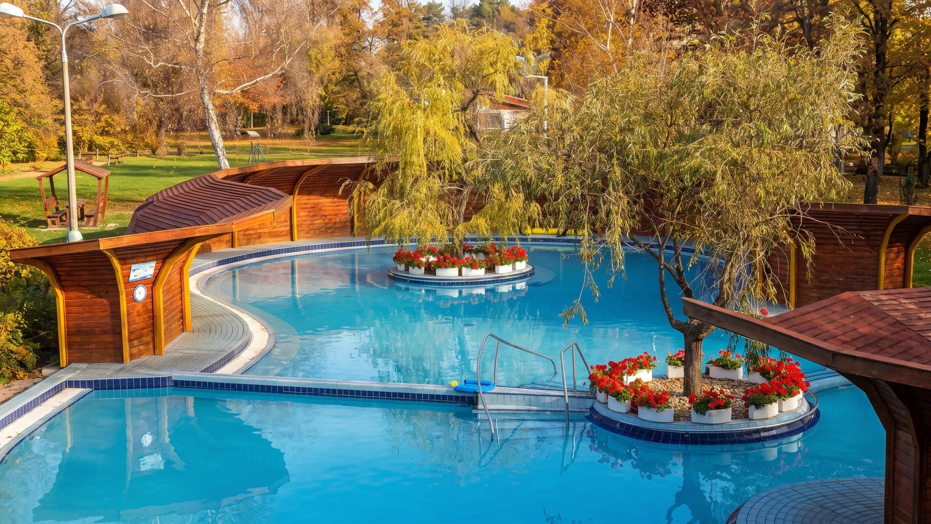 The curved outdoor pool at the Brigetio thermal bath in Komarom, screened by timber panels with planters of flowers in autumn.