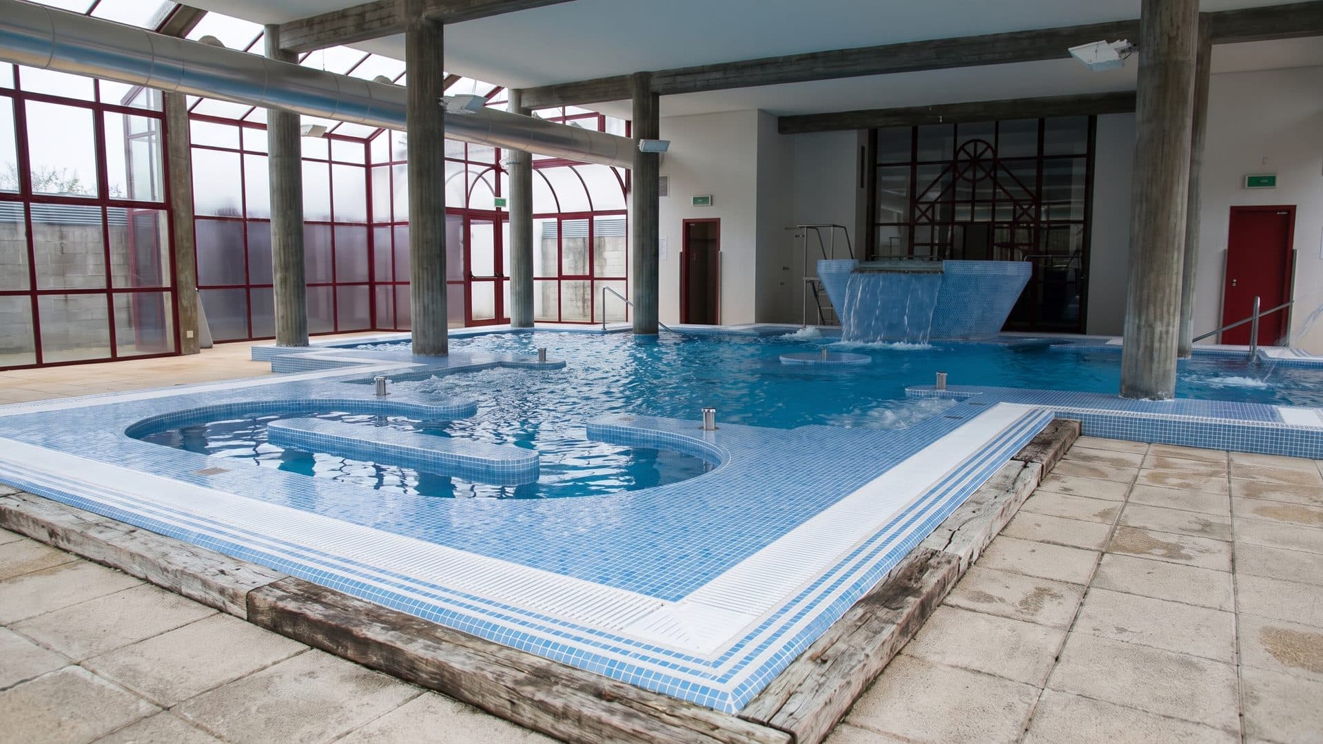 The indoor thermal pool at Caldas de Moncao with its stepped waterfall feature, under red-framed glazing