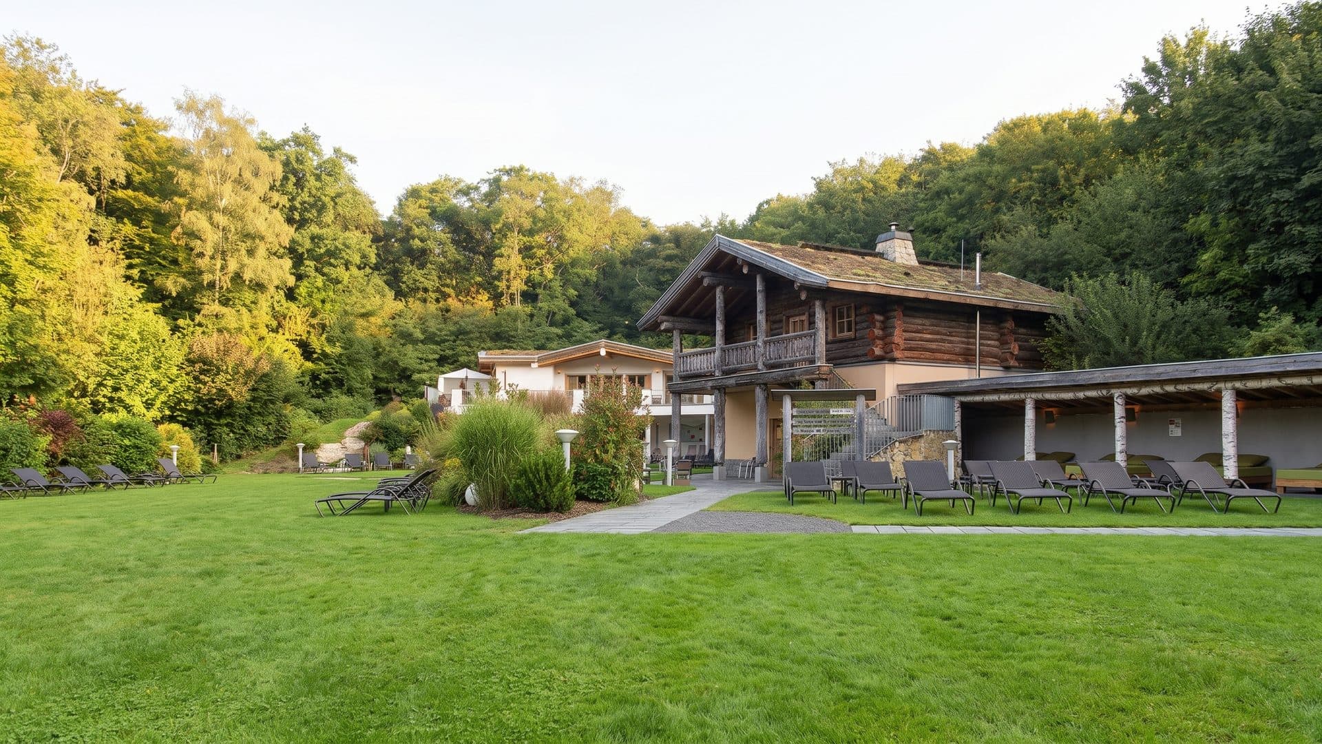 The timber lodge of the Calypso sauna garden seen across the lawn, loungers set out along the terrace