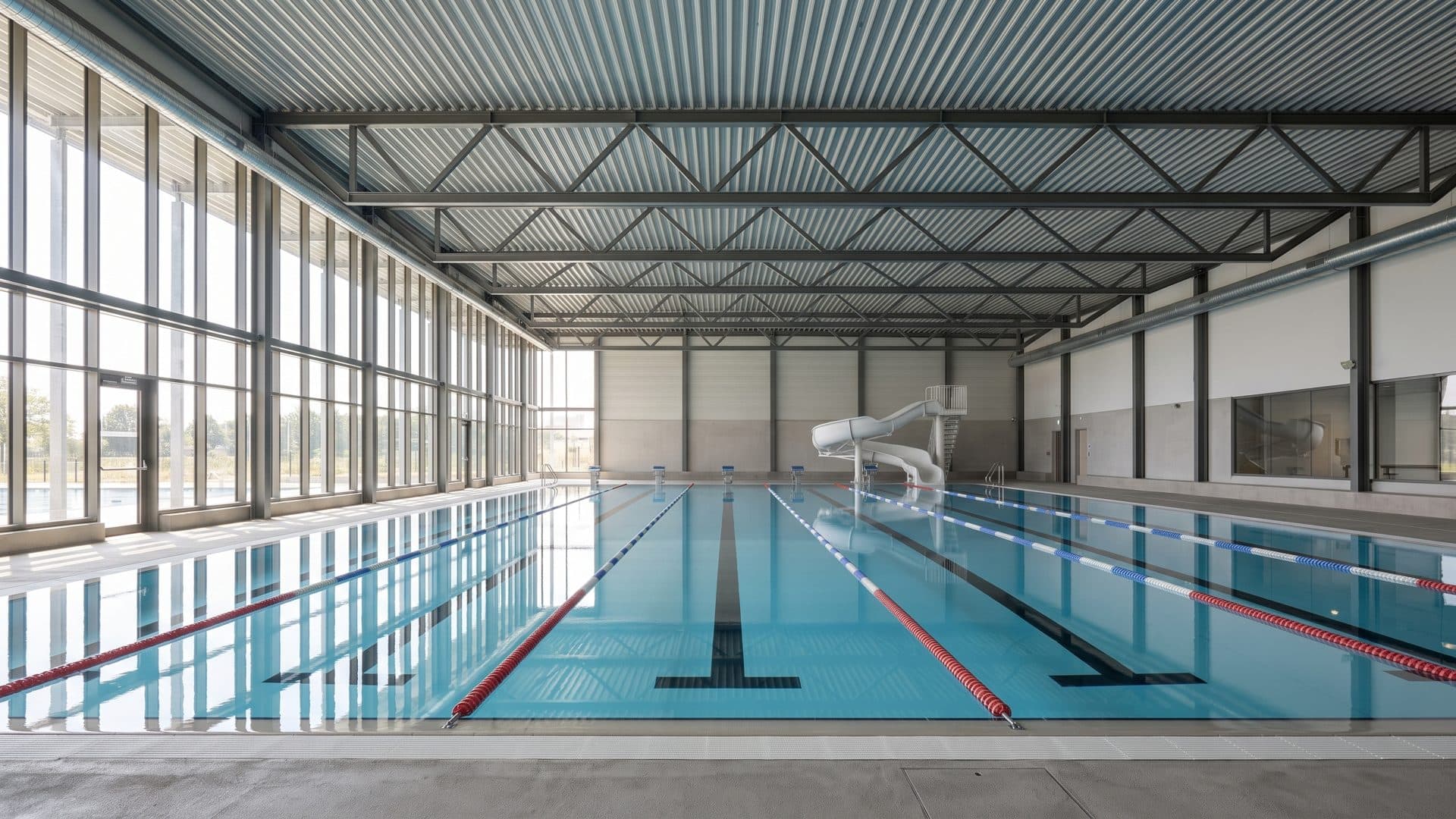 The lane pool of the Centre Aquatique Au Fil de l'O along its glazed wall under the steel roof
