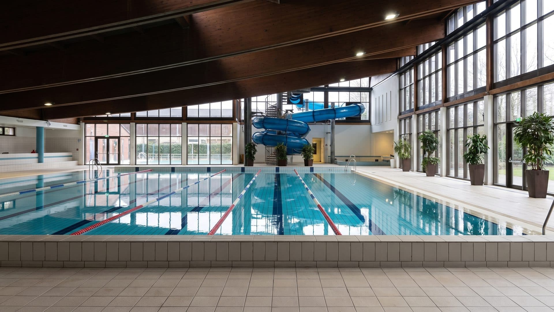 The lane pool of the Centro Acquatico di Cavalese under its timber ceiling beside the blue slide